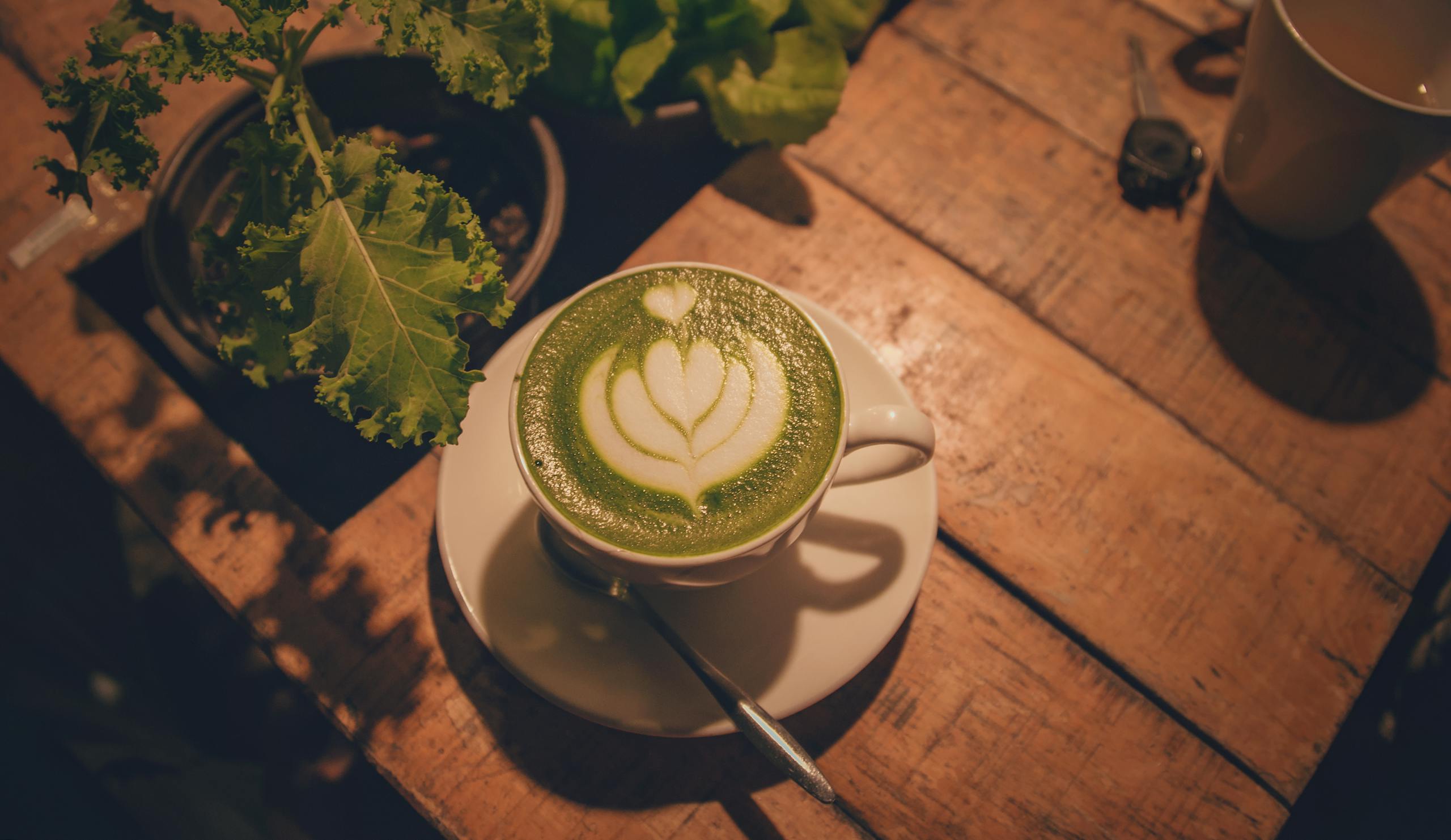A warm indoor scene of a matcha latte with beautiful latte art on a rustic wooden table.