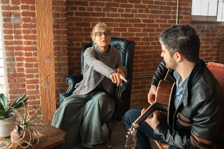 A woman and man share a relaxed moment indoors as he plays guitar and they converse.