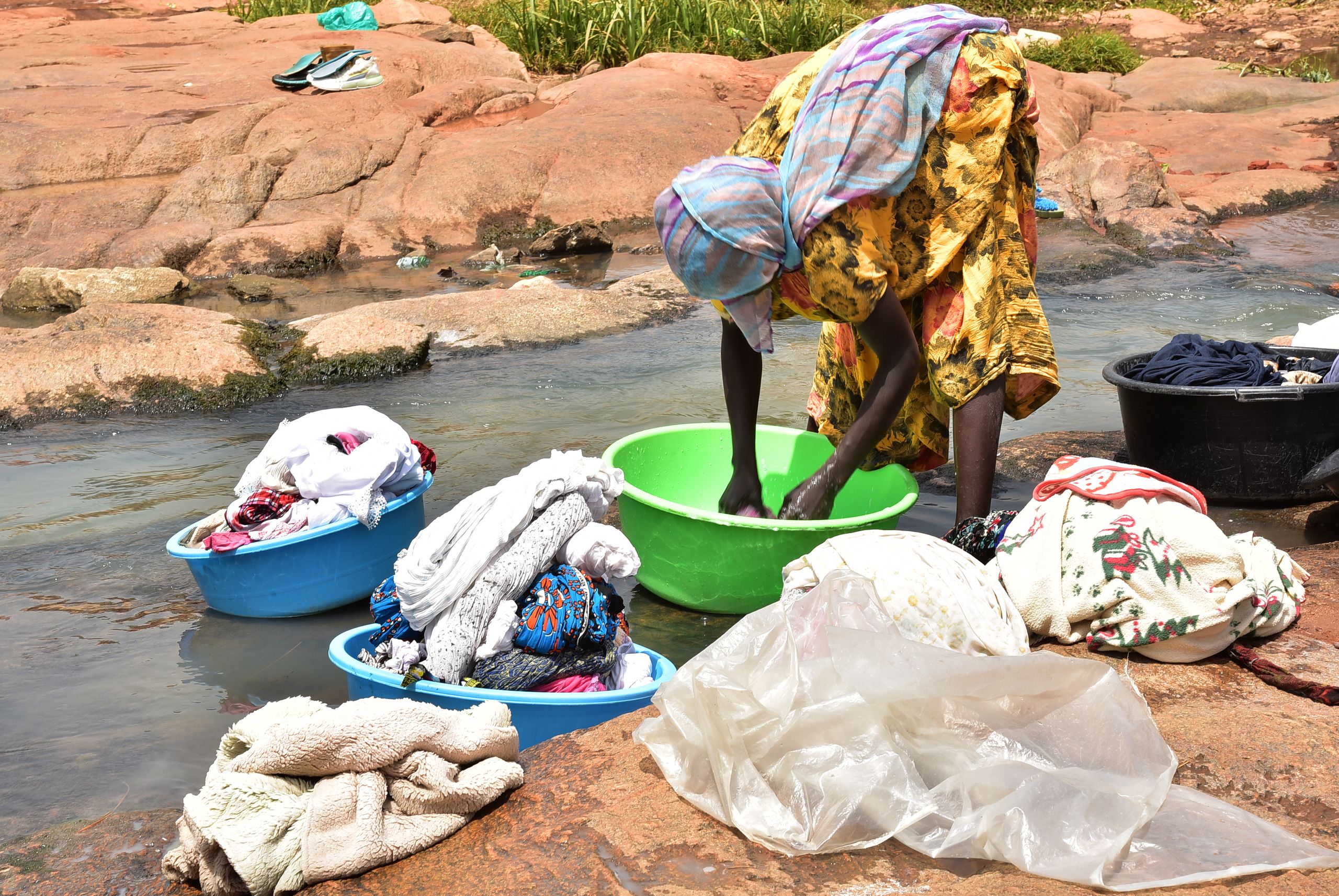 A woman doing laundry by a river, using colorful basins and traditional methods.