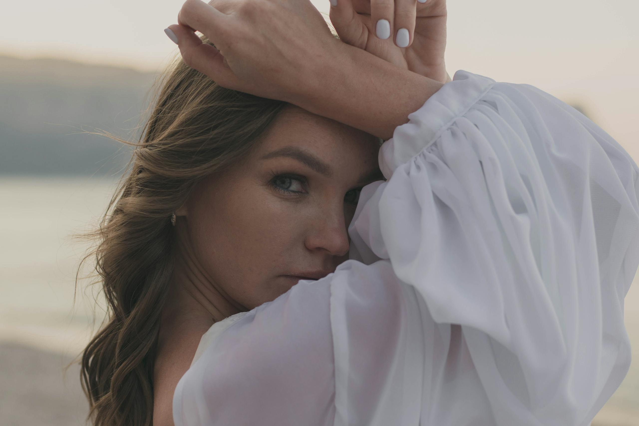 A woman in a white dress poses gracefully with a scenic sunset in the background.