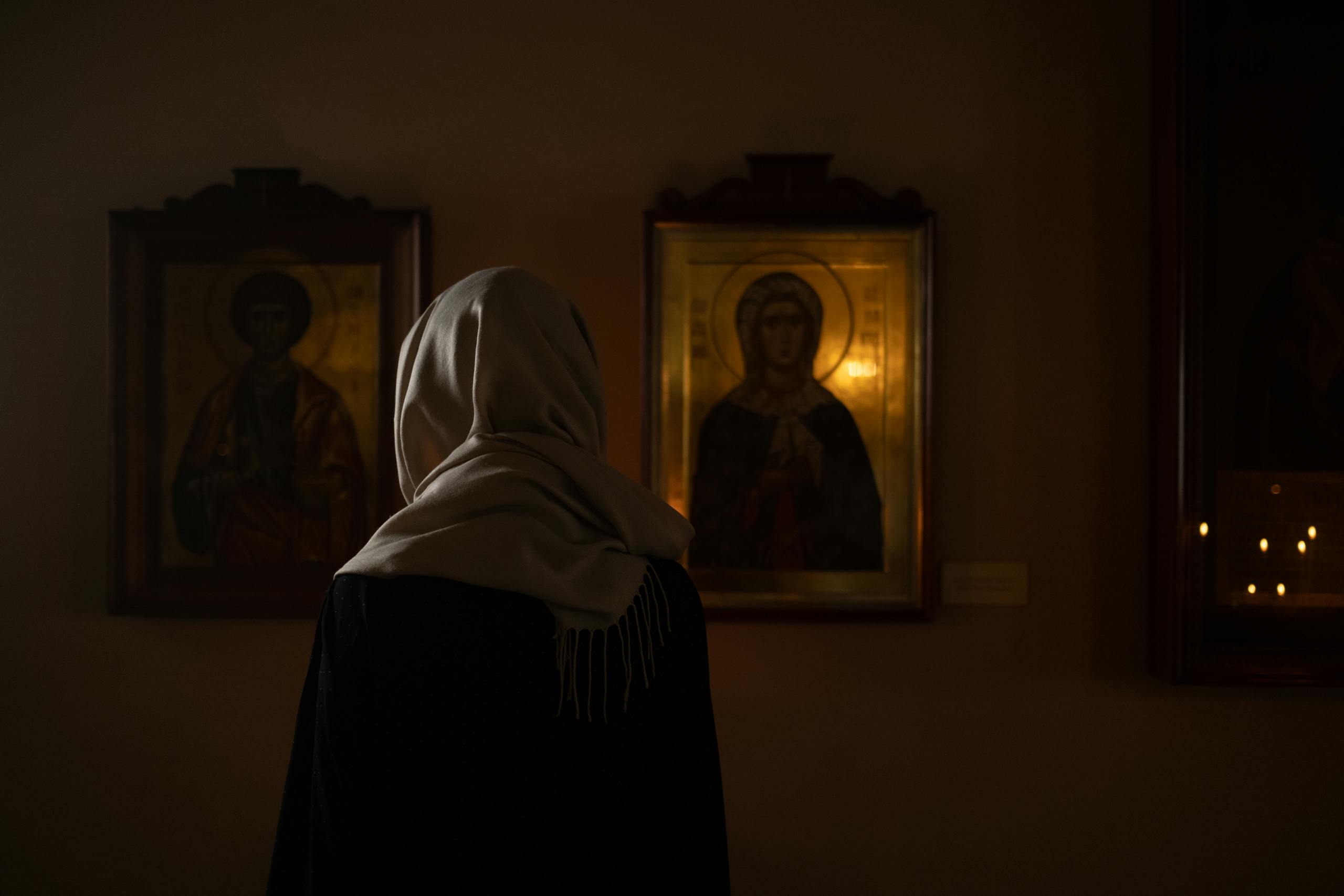A woman in headscarf stands before religious icons in a dimly lit church.
