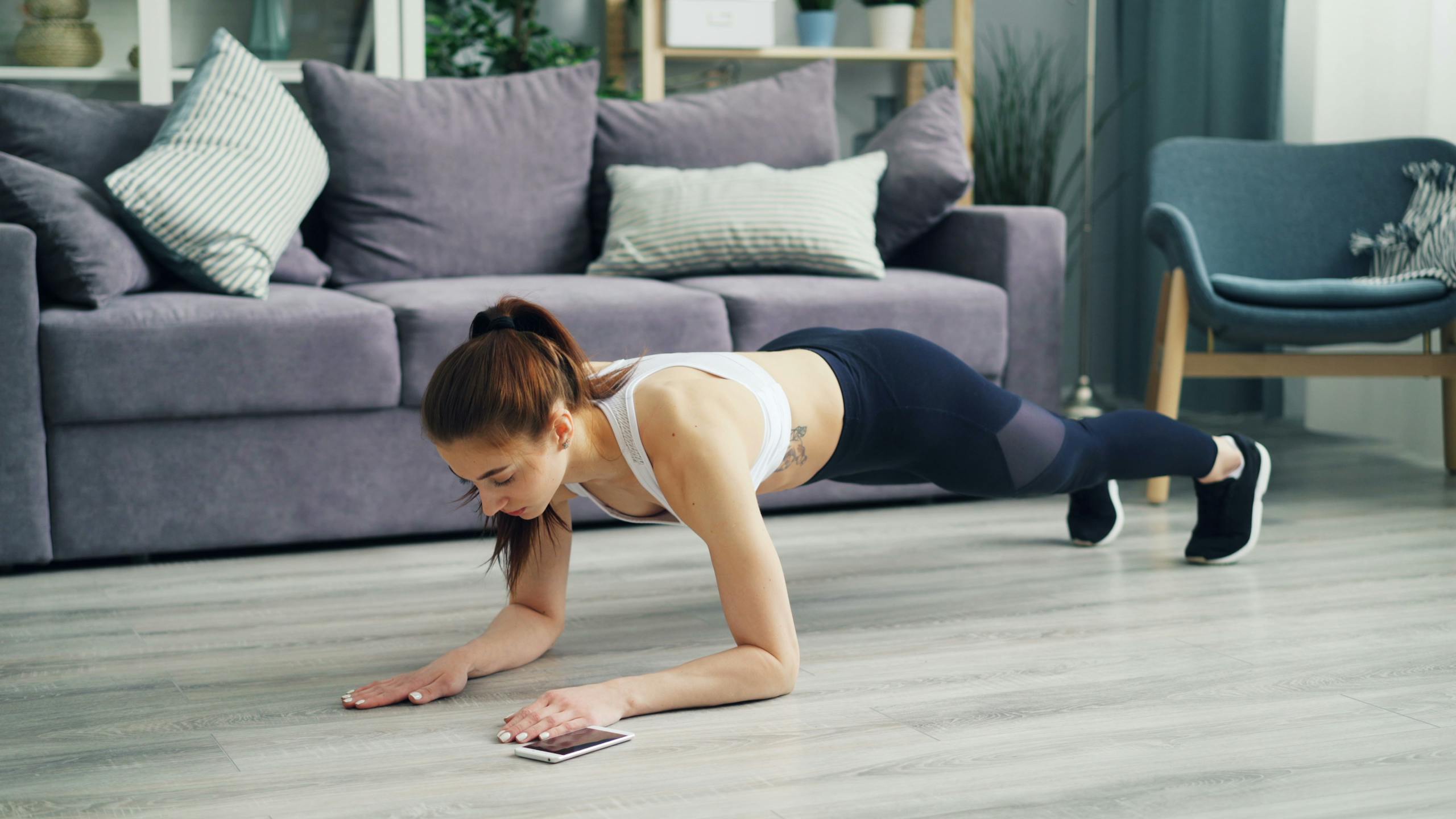 A woman performing a plank exercise in a modern living room setting.