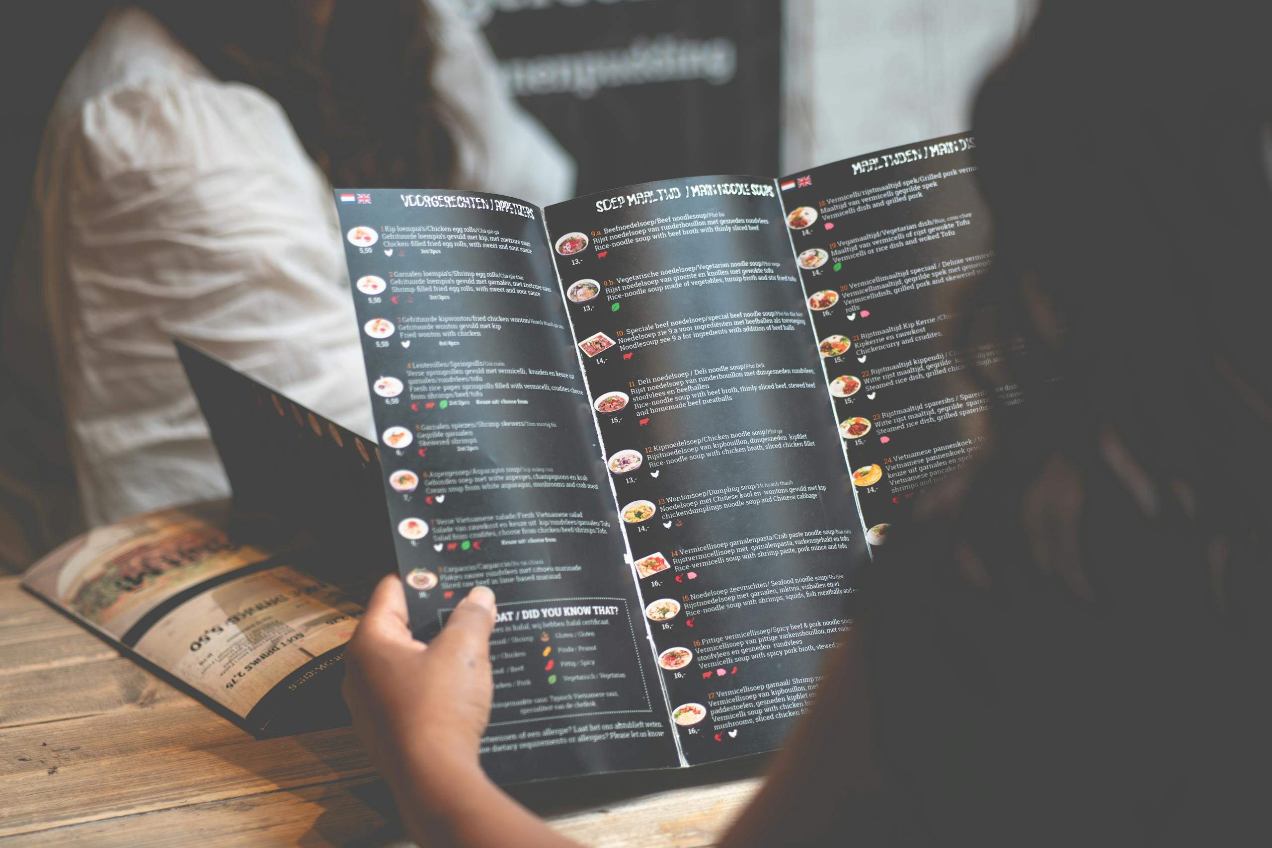 A woman reads a restaurant menu while sitting at a wooden table in Rotterdam.