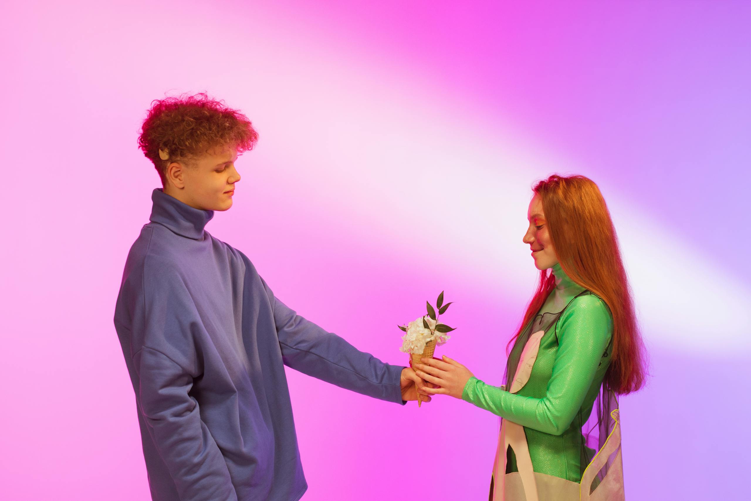 A young couple in a studio exchanging flowers on a colorful background.