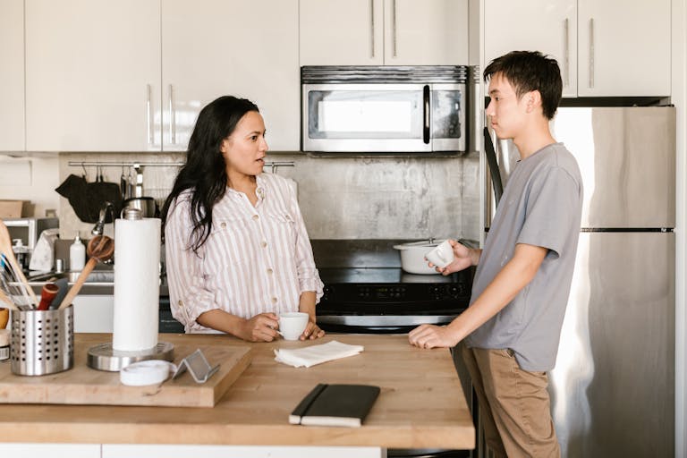 A young man and woman enjoy a casual talk over coffee in a sleek kitchen environment.