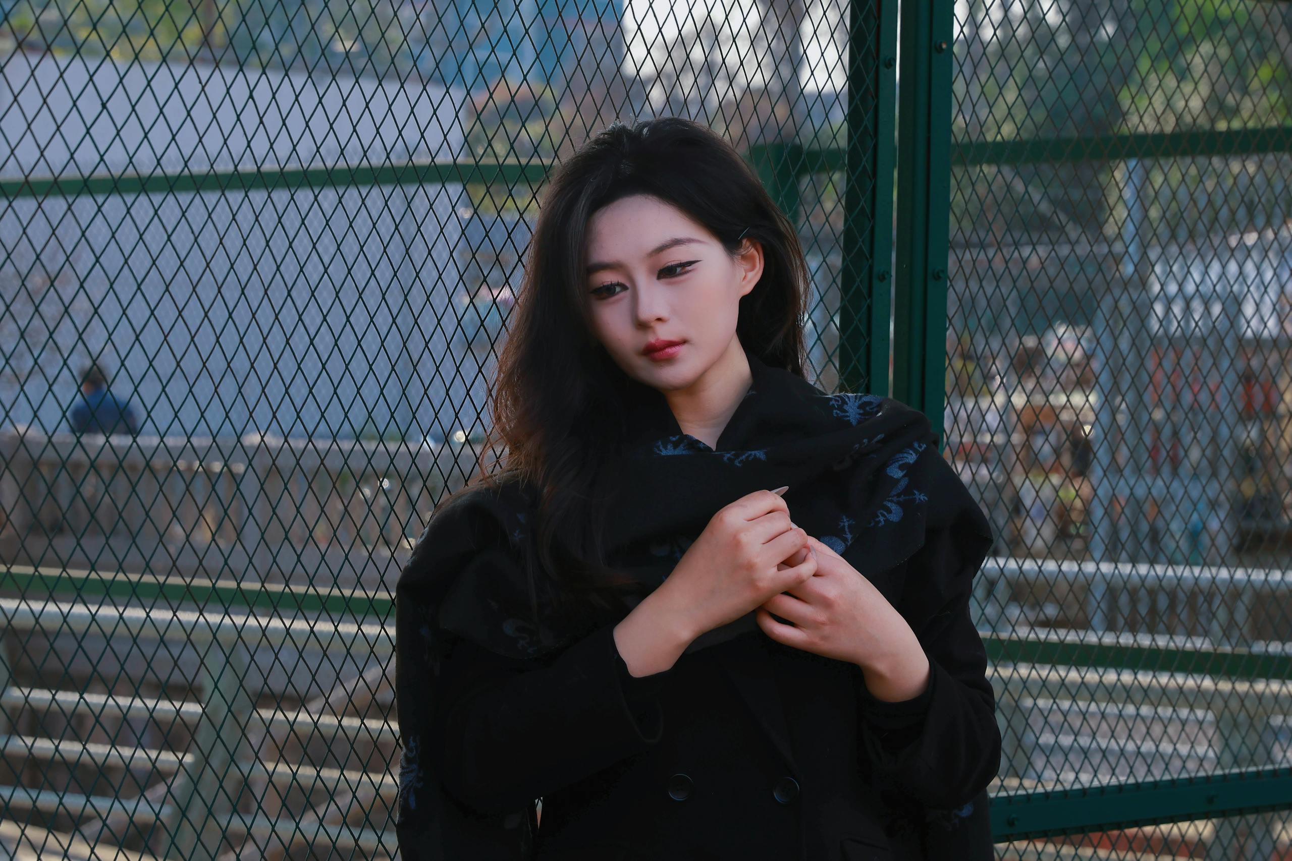 A young woman in a thoughtful pose by a city fence, expressing urban mood.
