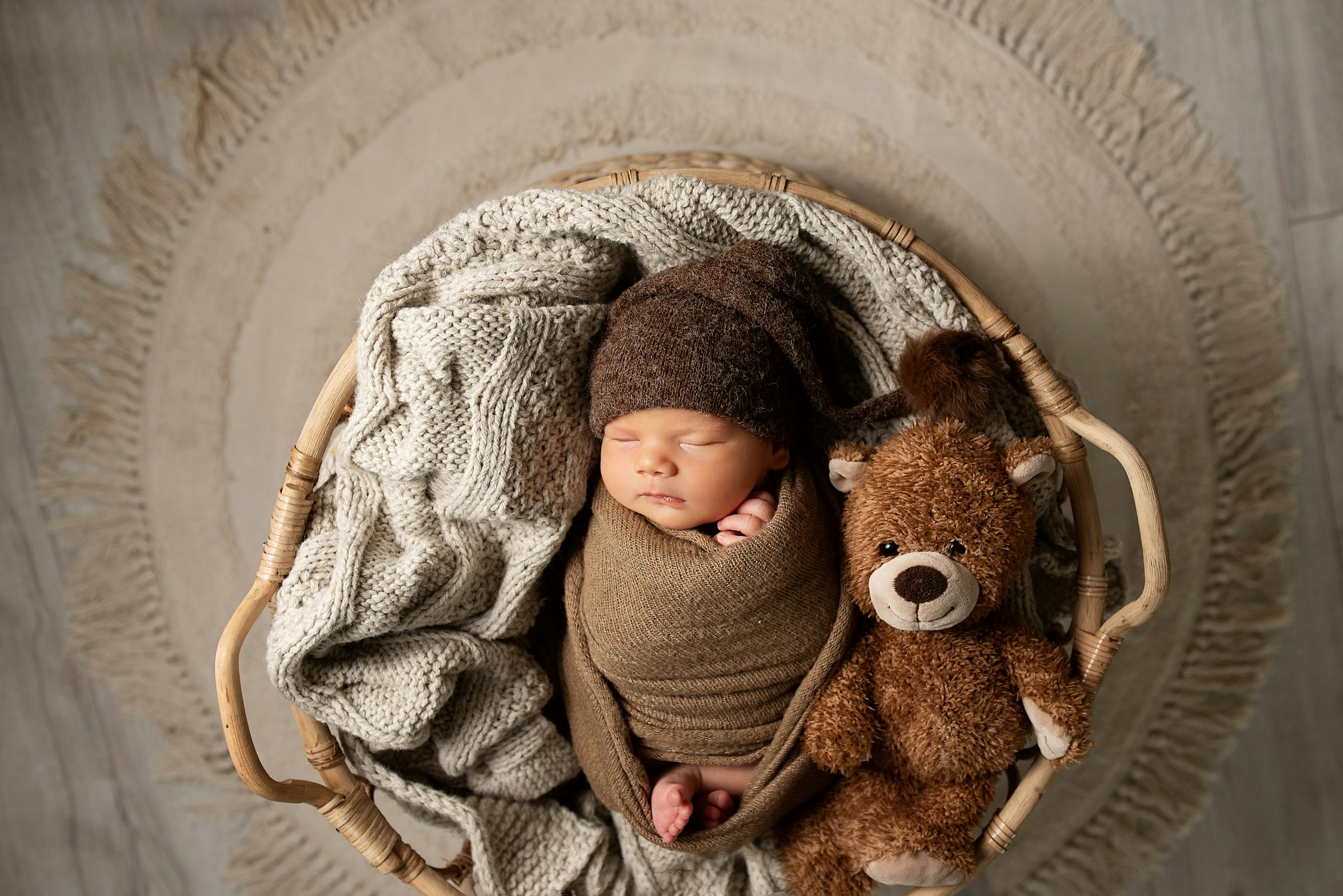 Adorable sleeping baby wrapped in soft blankets, cuddling a teddy bear.