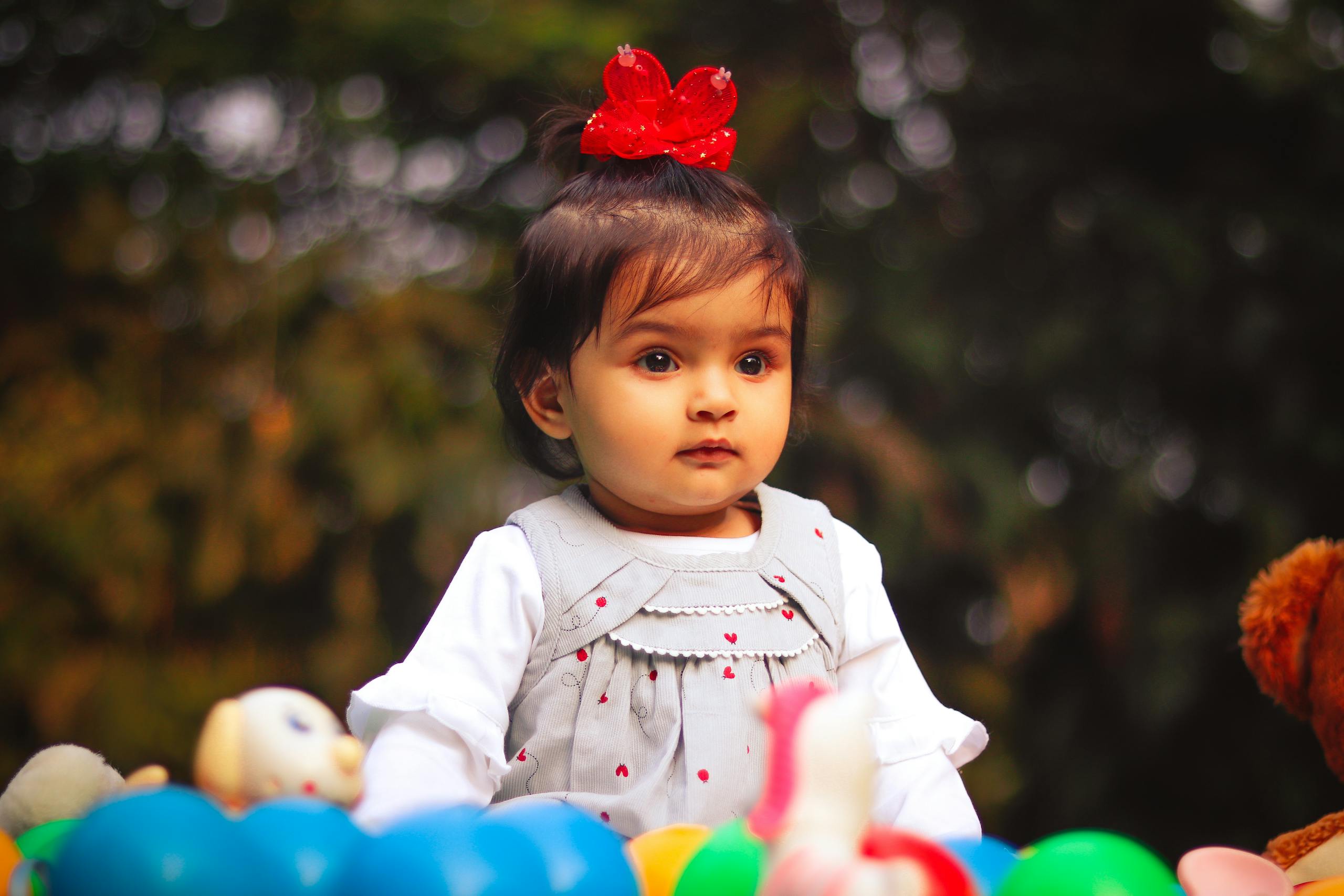 Adorable toddler girl with a red bow, playing with colorful toys in an outdoor setting.