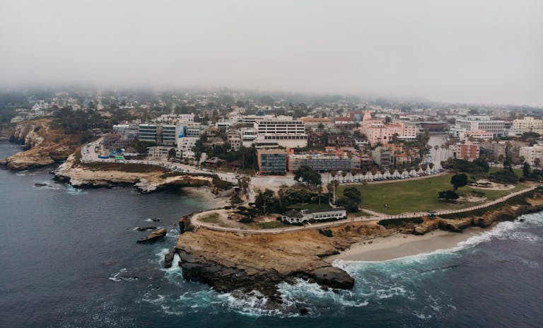 Aerial shot of La Jolla Cove in San Diego, California, showcasing coastal cliffs, cityscape, and foggy atmosphere.