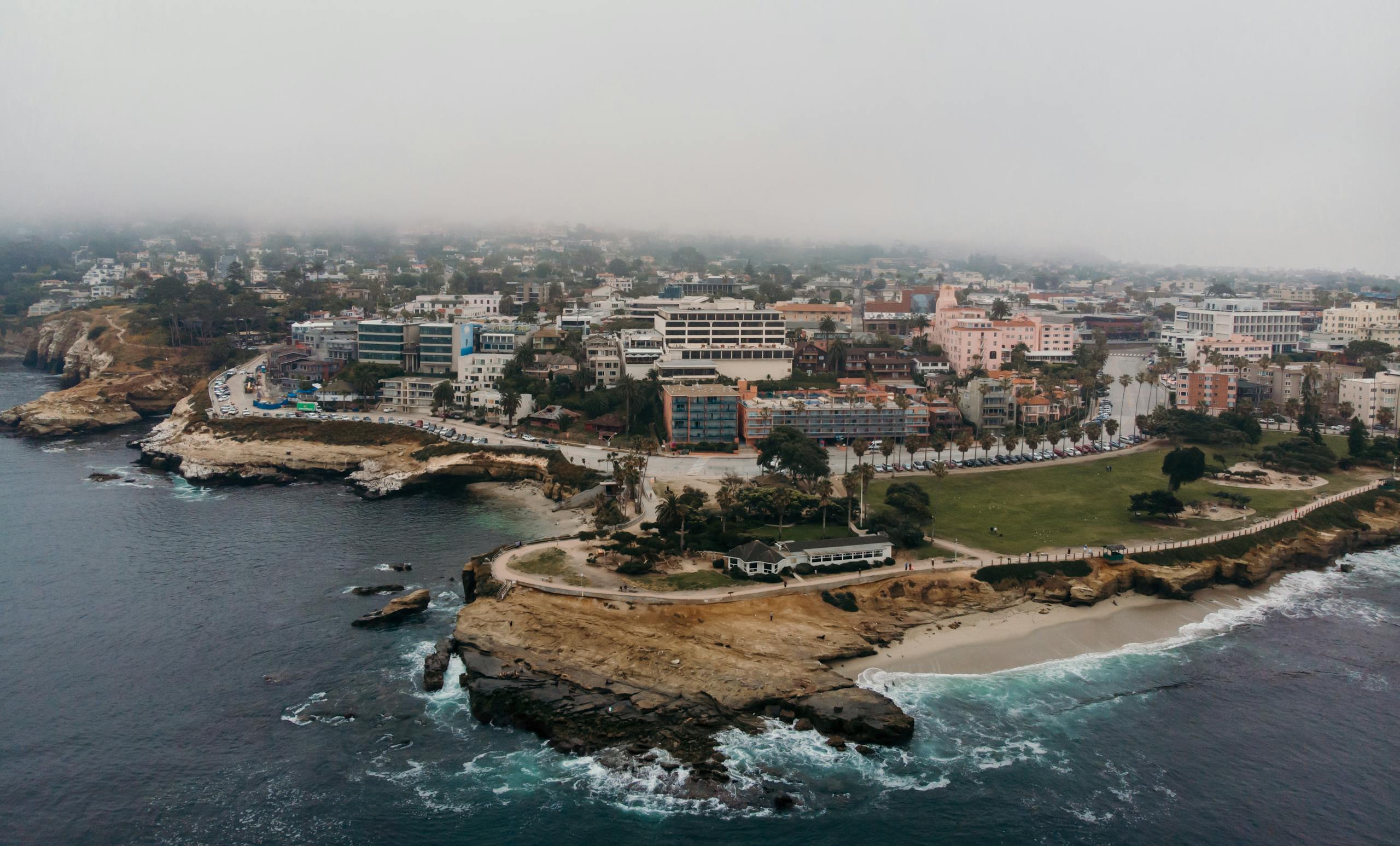 Aerial shot of La Jolla Cove in San Diego, California, showcasing coastal cliffs, cityscape, and foggy atmosphere.
