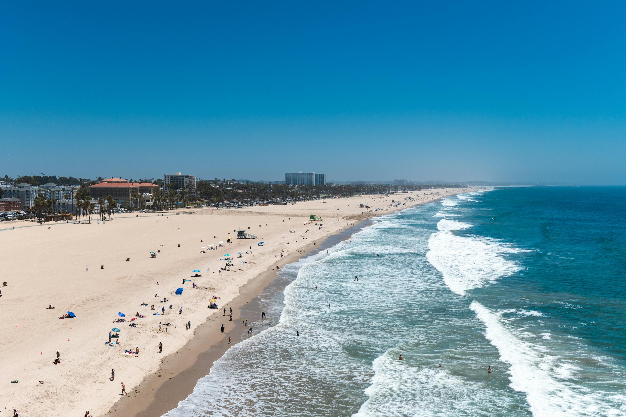 Aerial view of a lively beach scene at Santa Monica, capturing people enjoying the sun and sea.