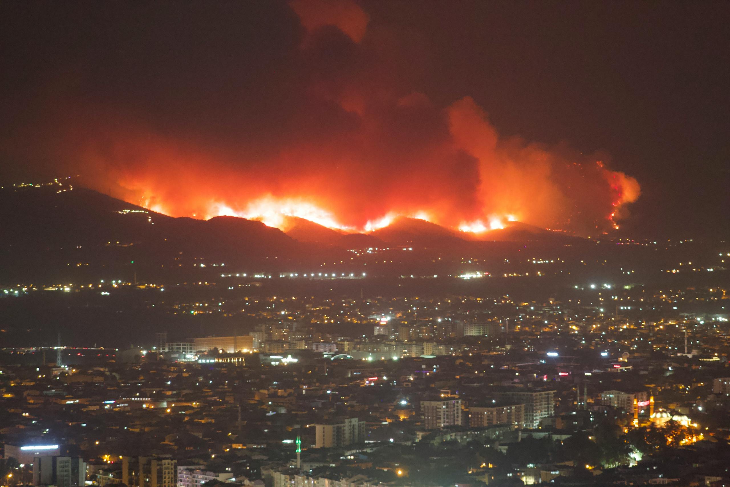 Aerial view of city with blazing wildfires illuminating the night sky.