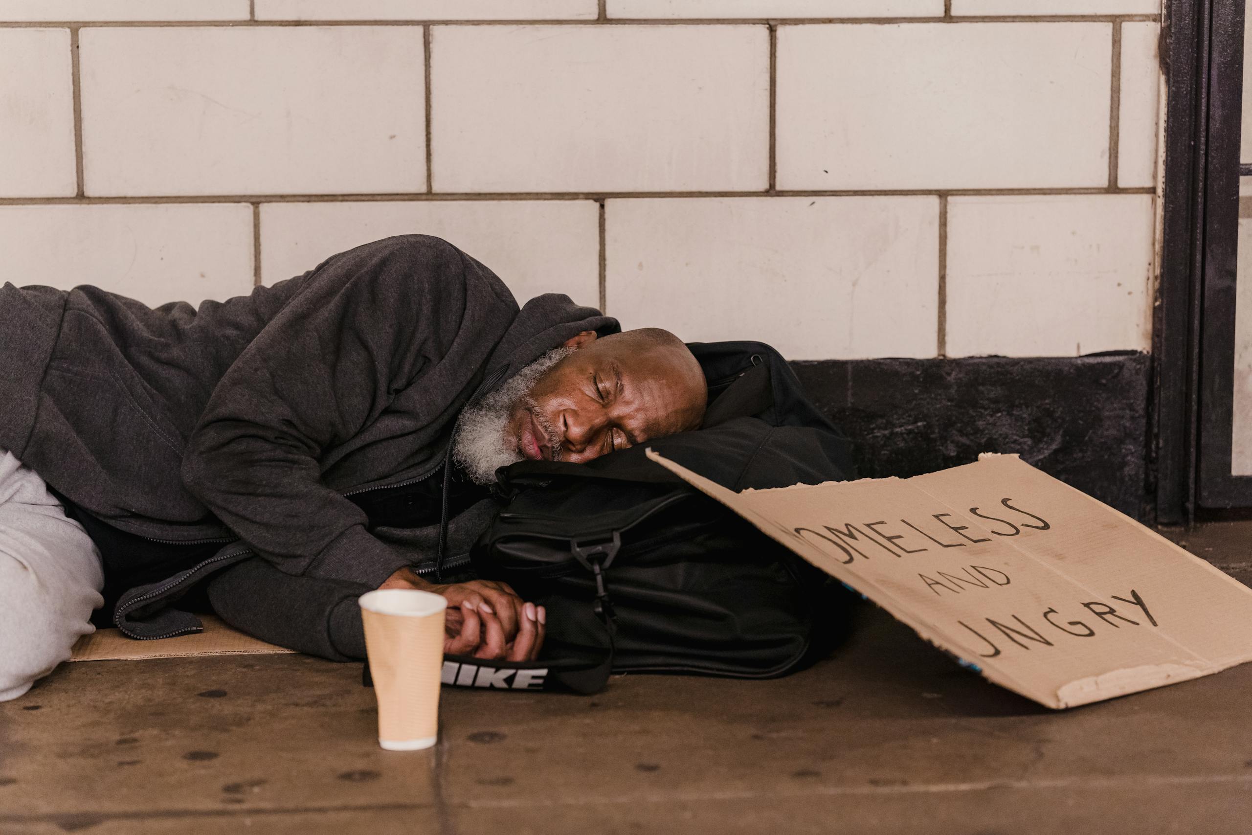 African American man sleeping in subway with sign, highlighting social issues.
