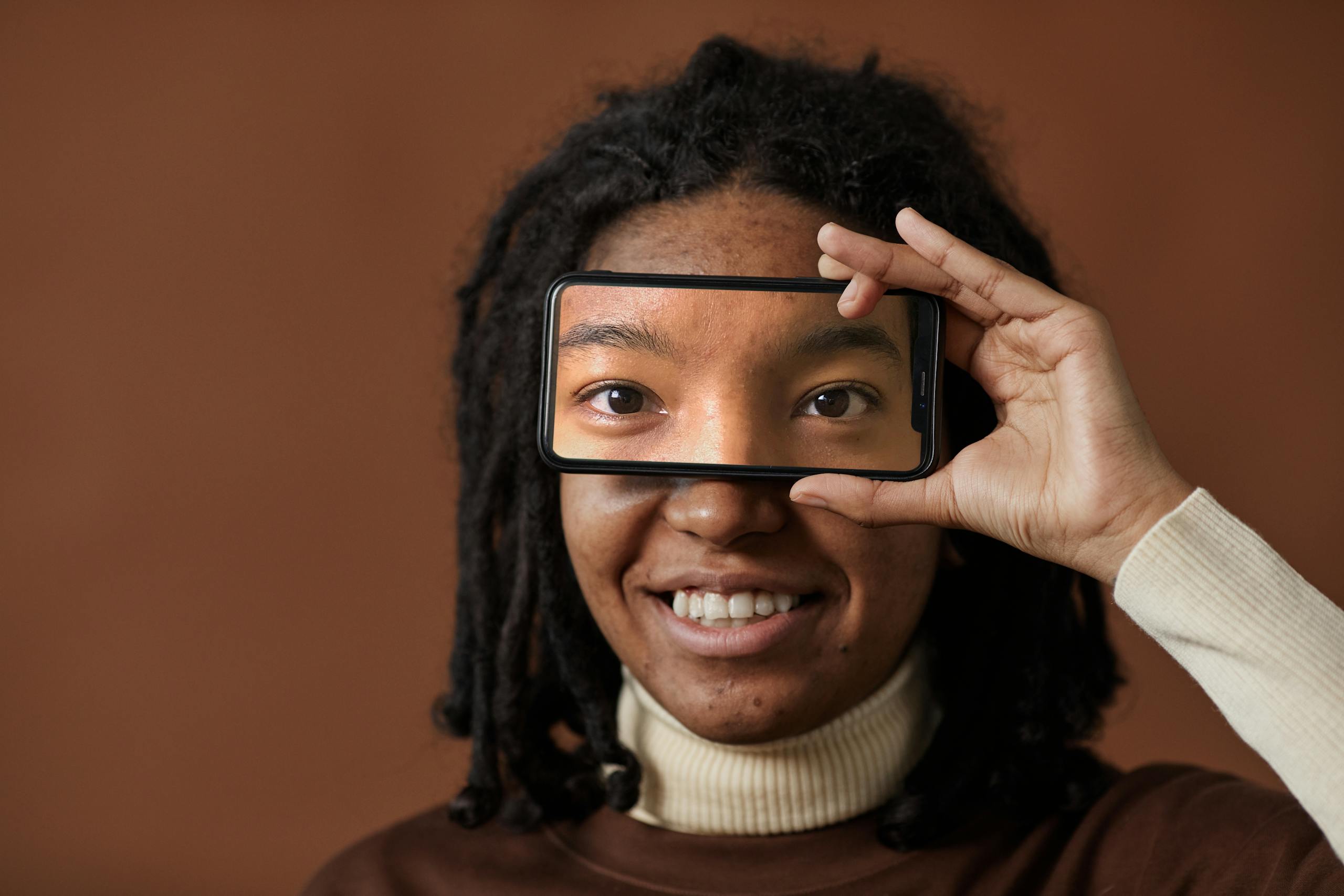 African woman smiling and holding smartphone to eyes in studio.