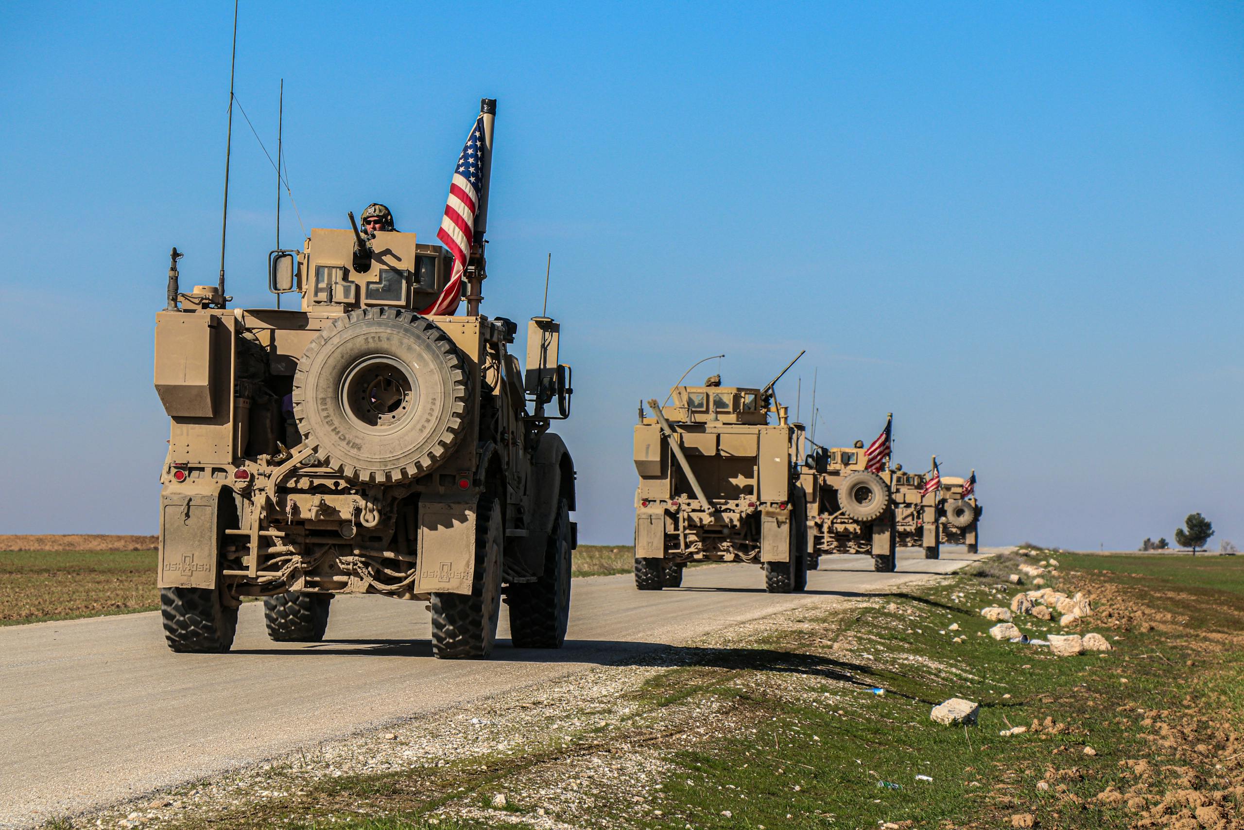American military convoy driving through rural Syria under a blue sky.