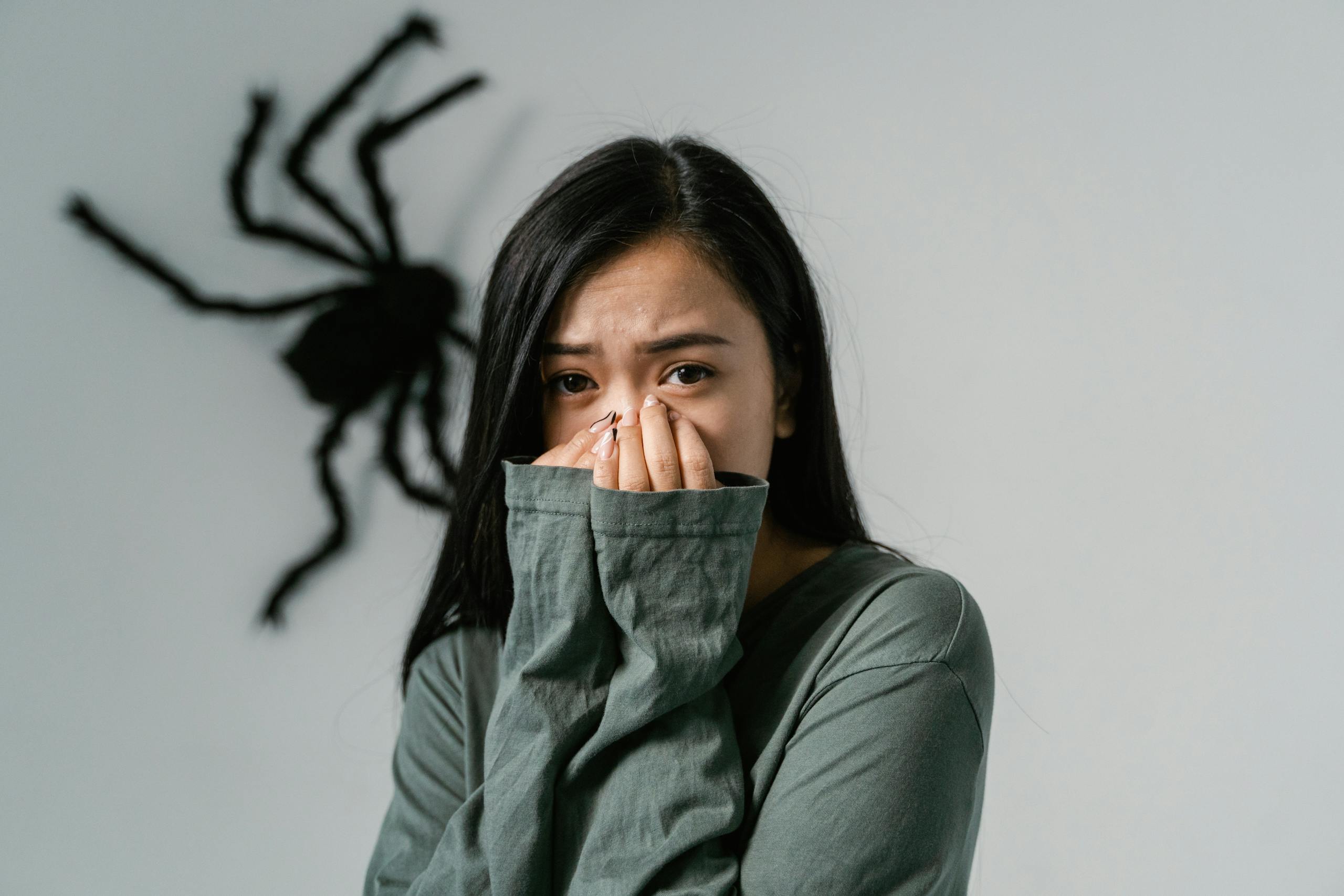 An anxious woman indoors with a large wall spider, depicting arachnophobia.
