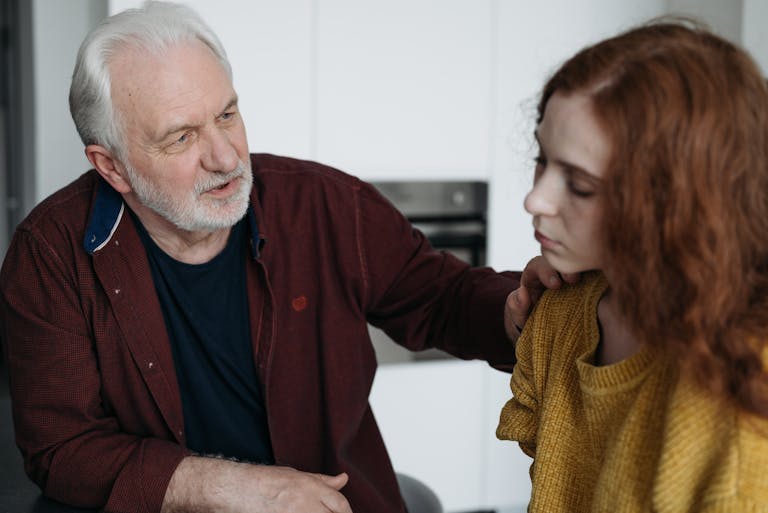 An elderly man consoles a young woman indoors, expressing empathy and understanding.