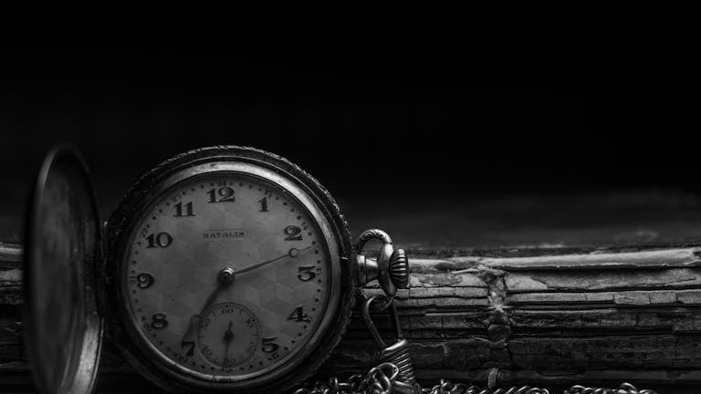 Antique pocket watch resting on a vintage book in black and white.