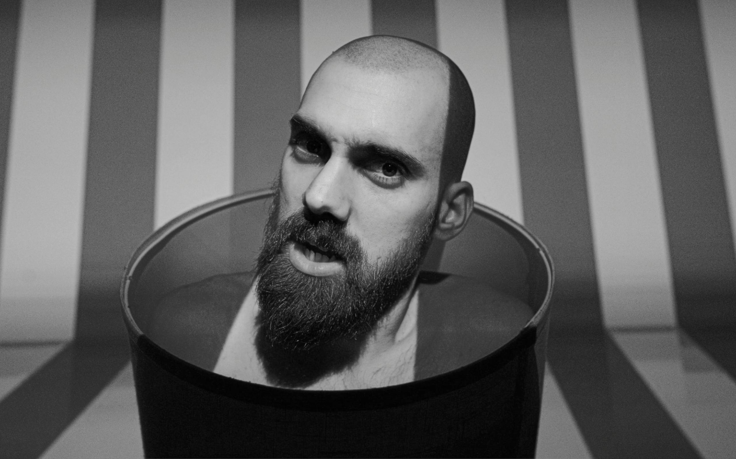 Artistic black and white portrait of a bearded man emerging from a bucket with a striped background.