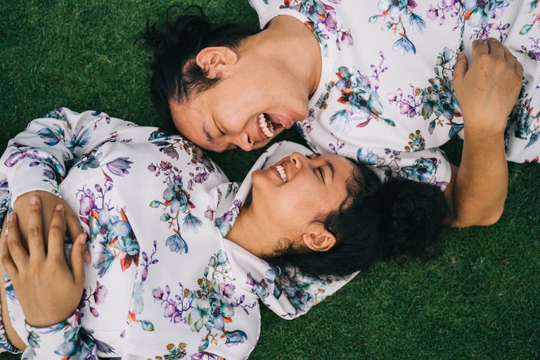 Asian couple in matching floral co-ord sets laughing together on grass, symbolizing happiness.