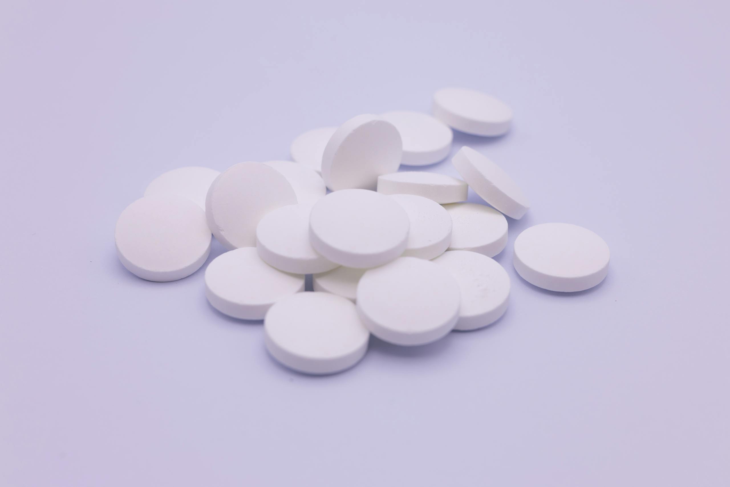 Assorted white tablets stacked on a soft purple surface, symbolizing medication and healthcare.