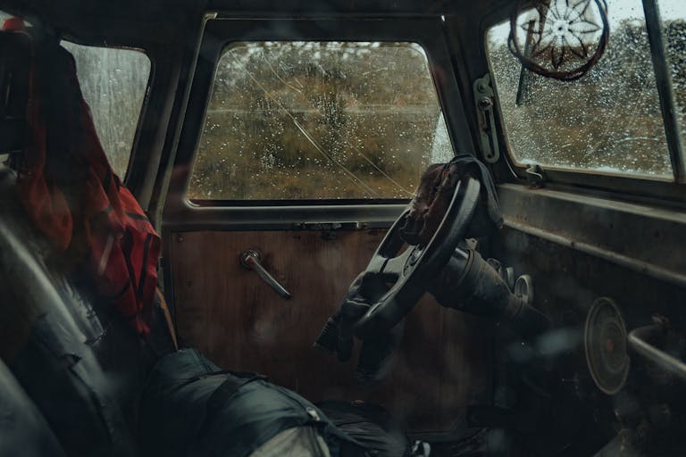 Atmospheric view of a vintage car interior with rain-soaked windows and worn textures.