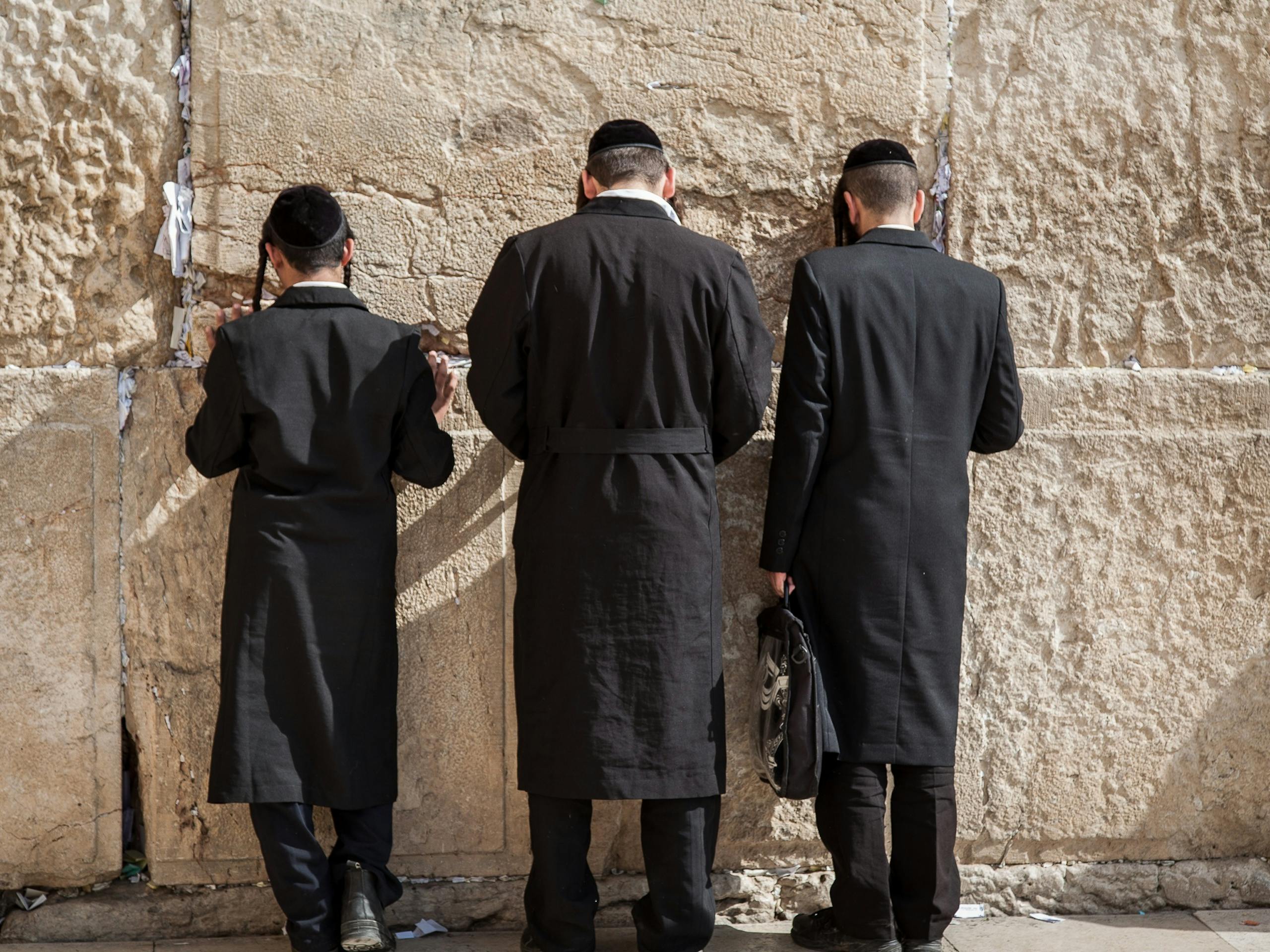 Back view of unrecognizable orthodox Jewish men in traditional religious clothes praying against Western Wall in Old City of Jerusalem