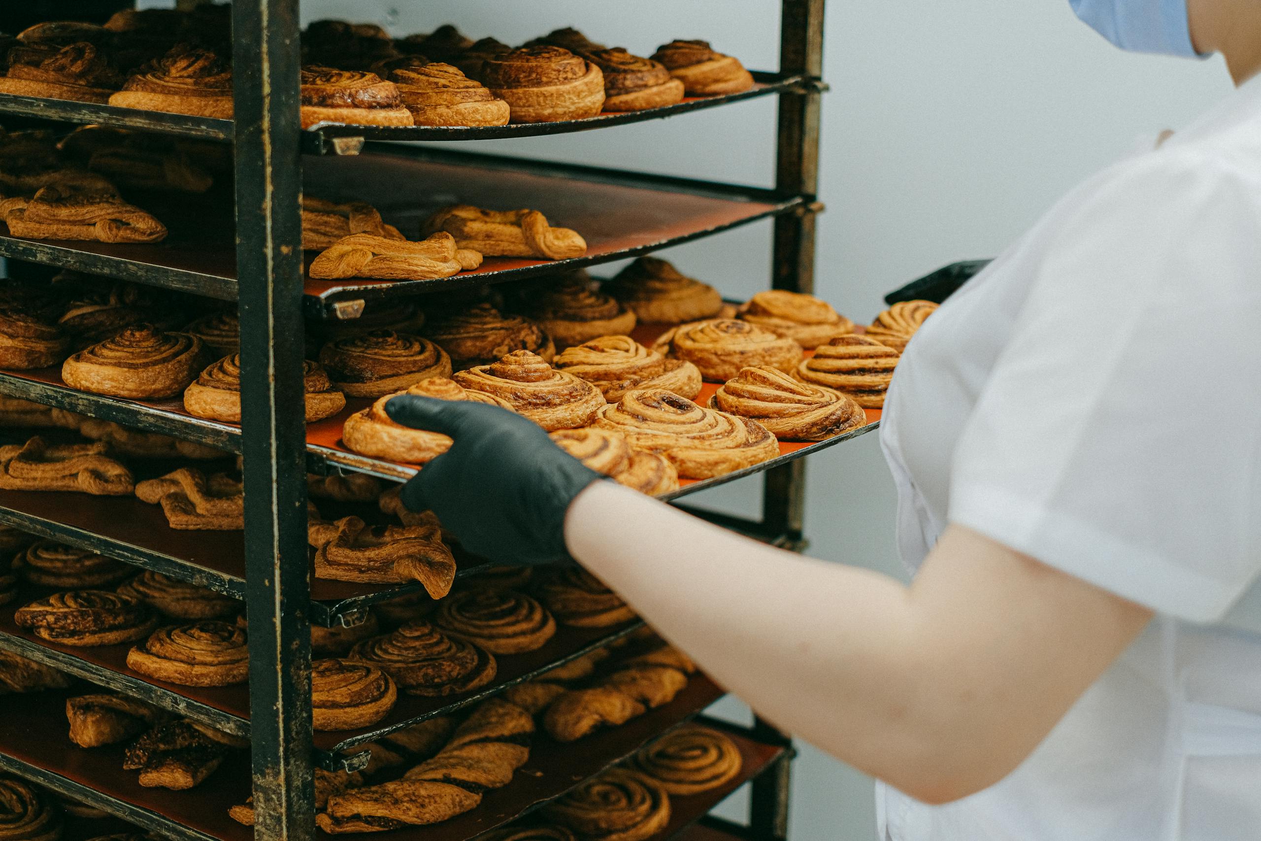 Baker placing freshly baked cinnamon rolls on a cooling rack in a bakery kitchen.
