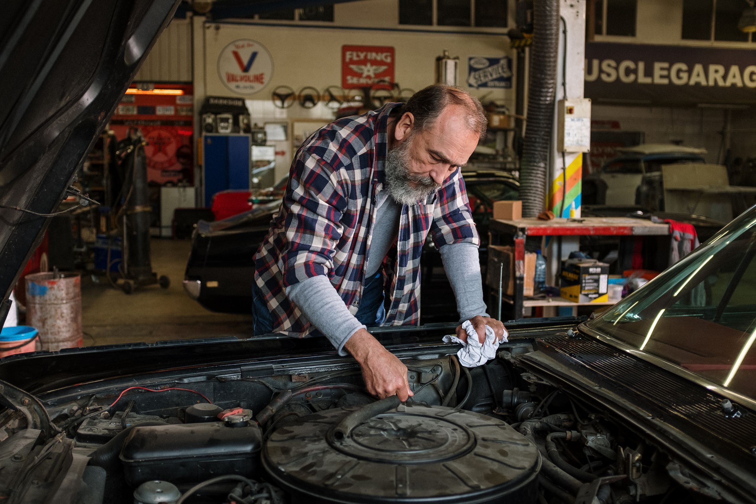 Bearded mechanic working on engine repair in an auto repair shop garage with a focus on hands-on car service.