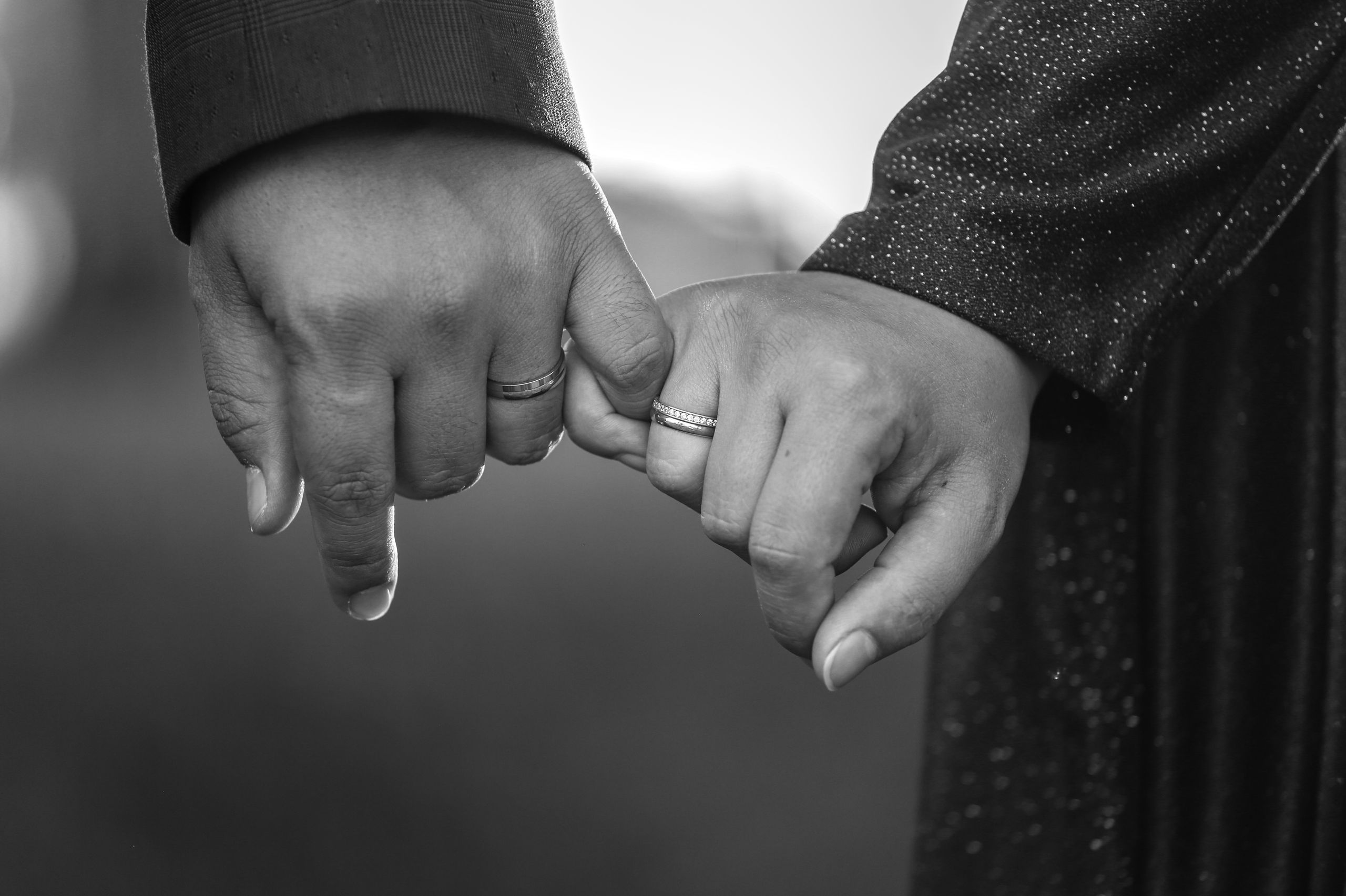 Black and white image of couple holding hands, showcasing engagement rings, symbolizing commitment and love.