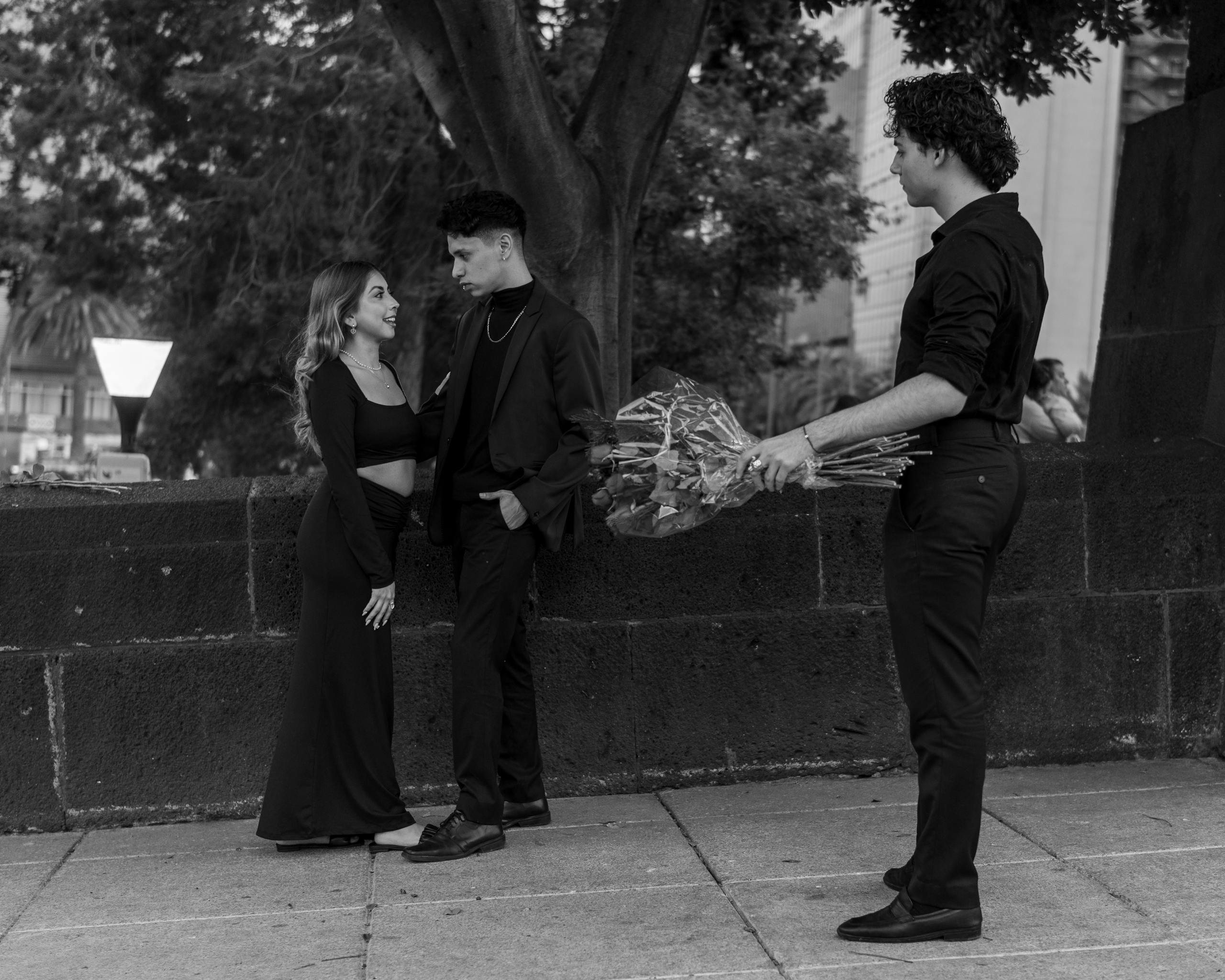 Black and white photo of a love triangle with emotional tension outdoors.
