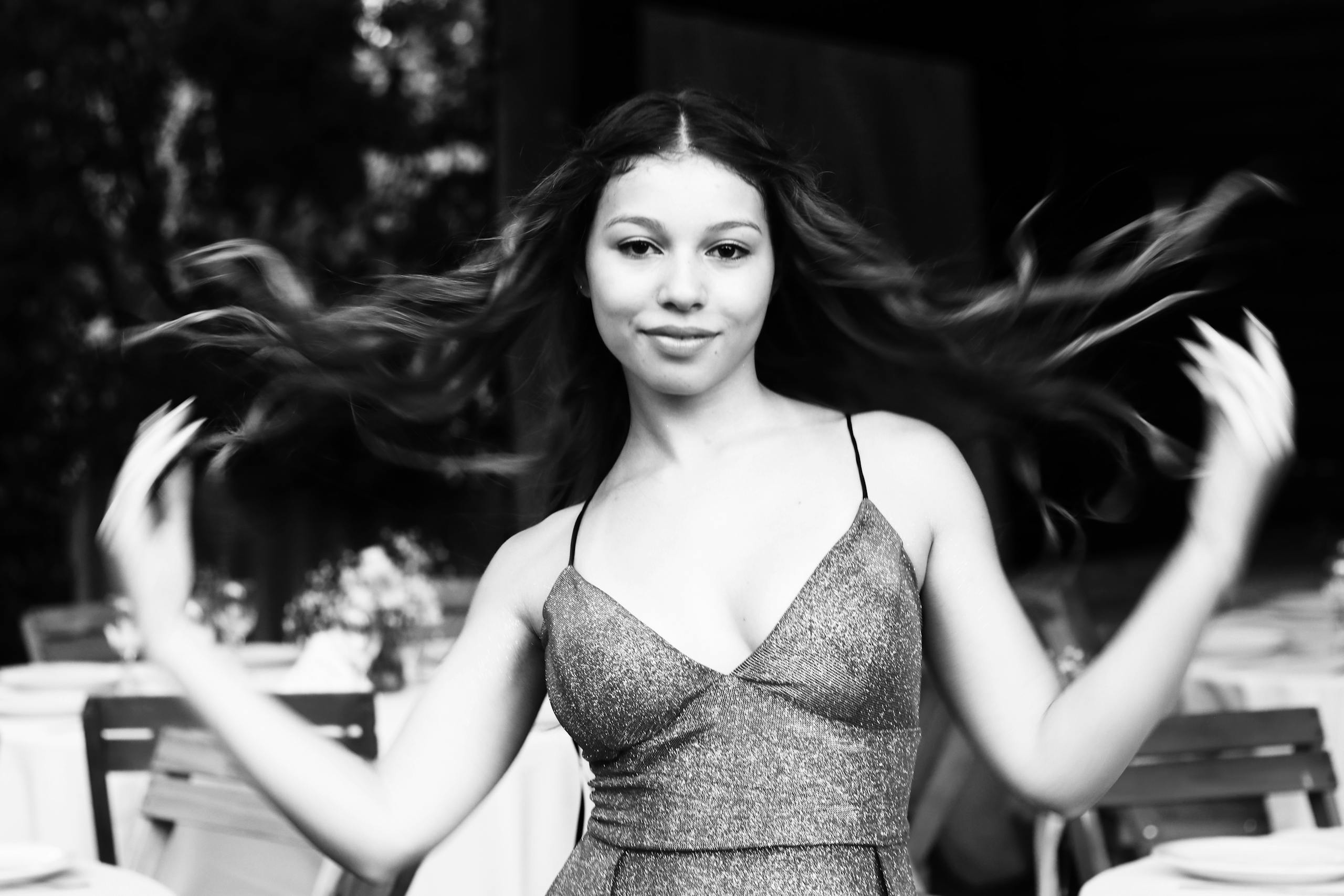 Black and white portrait of a smiling woman elegantly twirling outdoors.