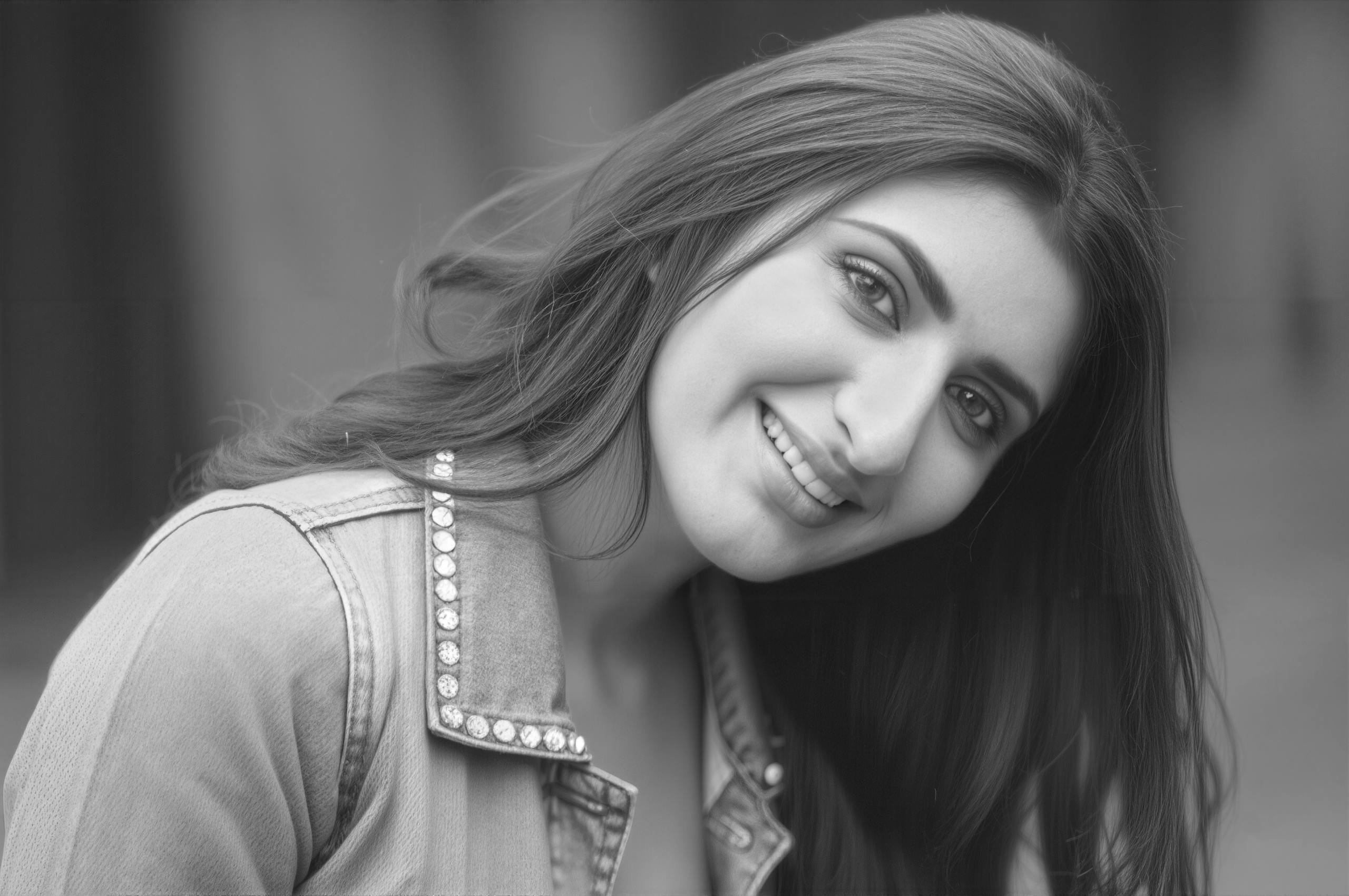 Black and white portrait of a smiling woman in a denim jacket, exuding casual elegance.