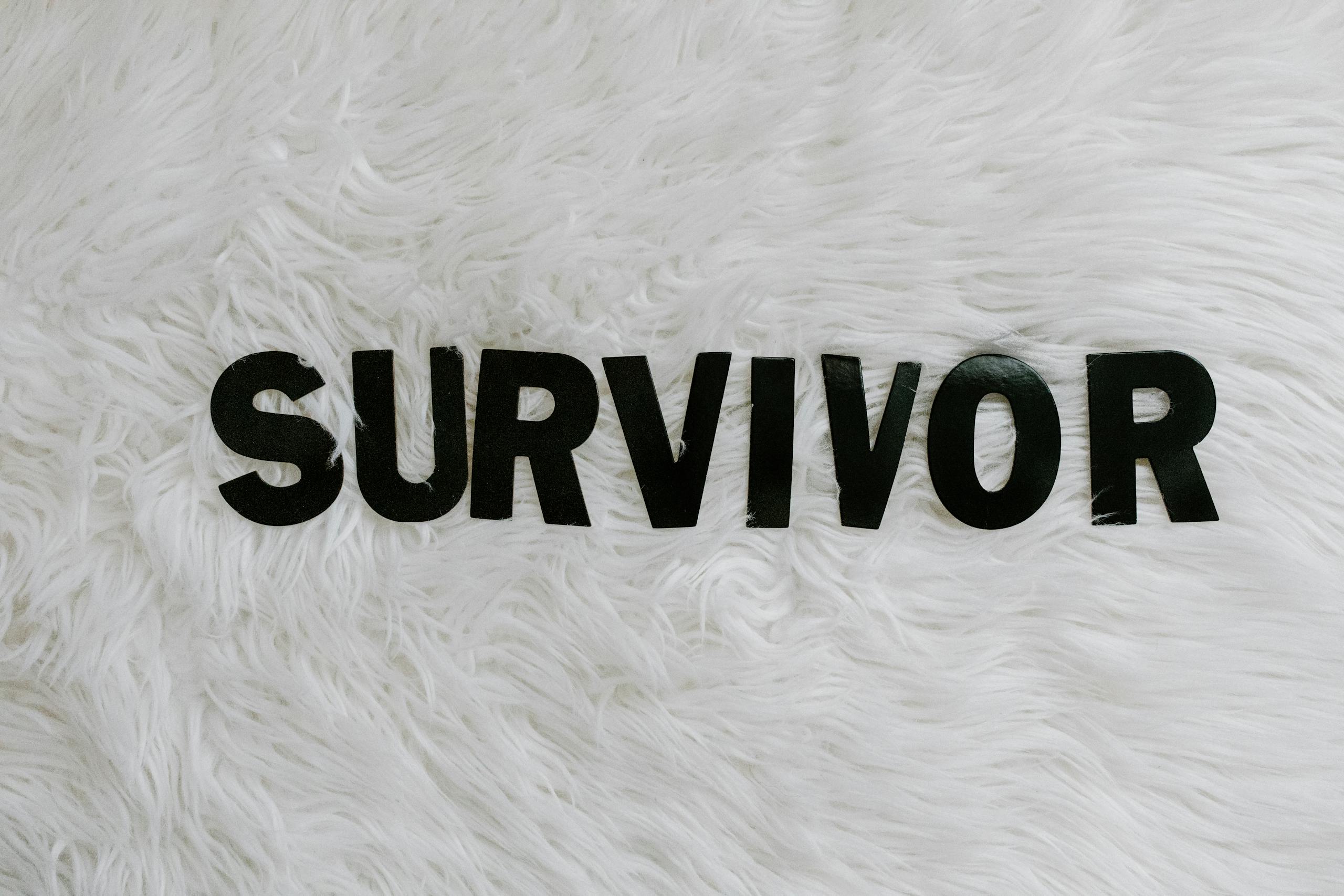 Black letters spelling 'SURVIVOR' on a white textured surface, symbolizing resilience.
