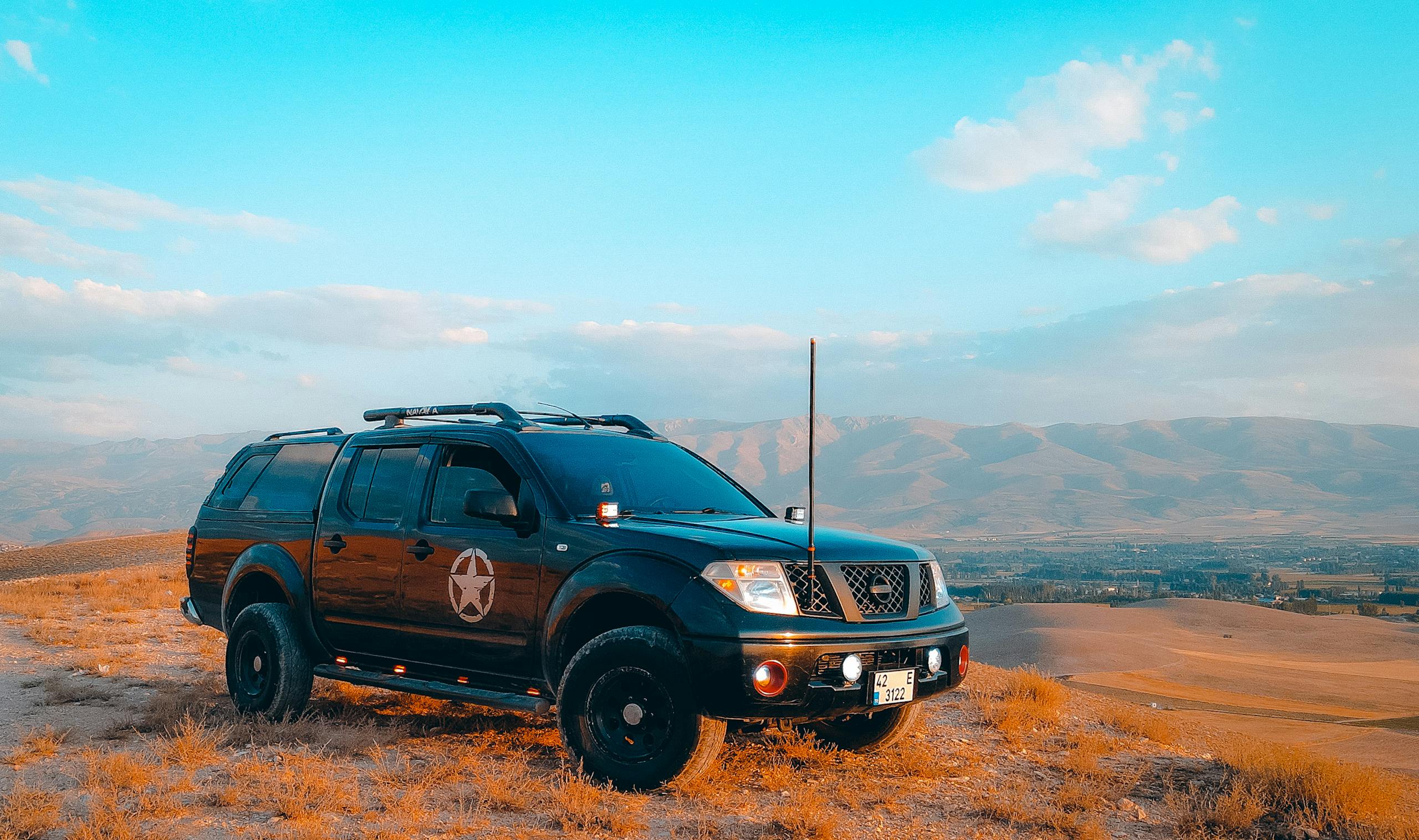Black SUV parked on a hill with mountains in the background under a blue sky.
