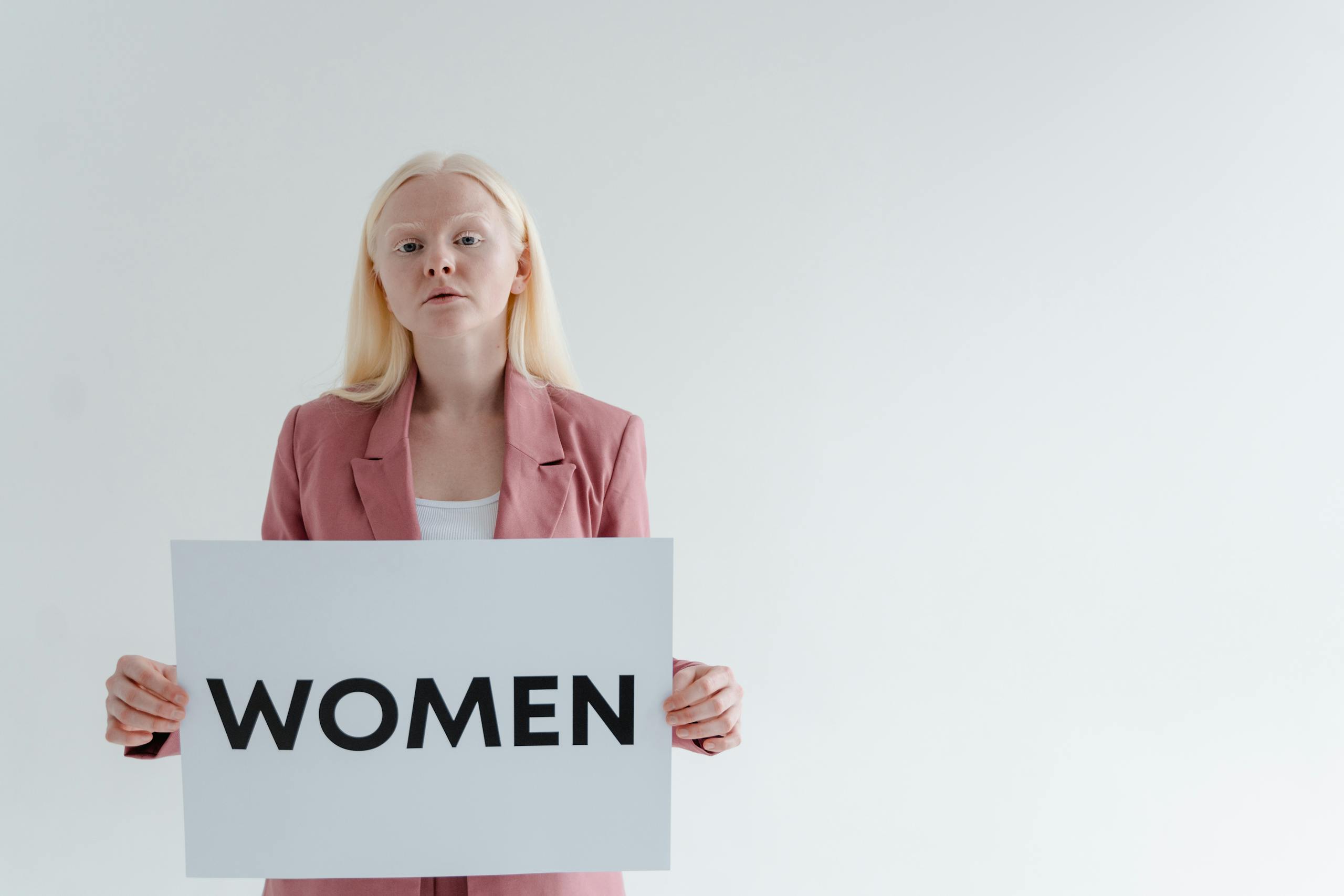 Blonde woman holding a sign with the word 'WOMEN' in a studio.