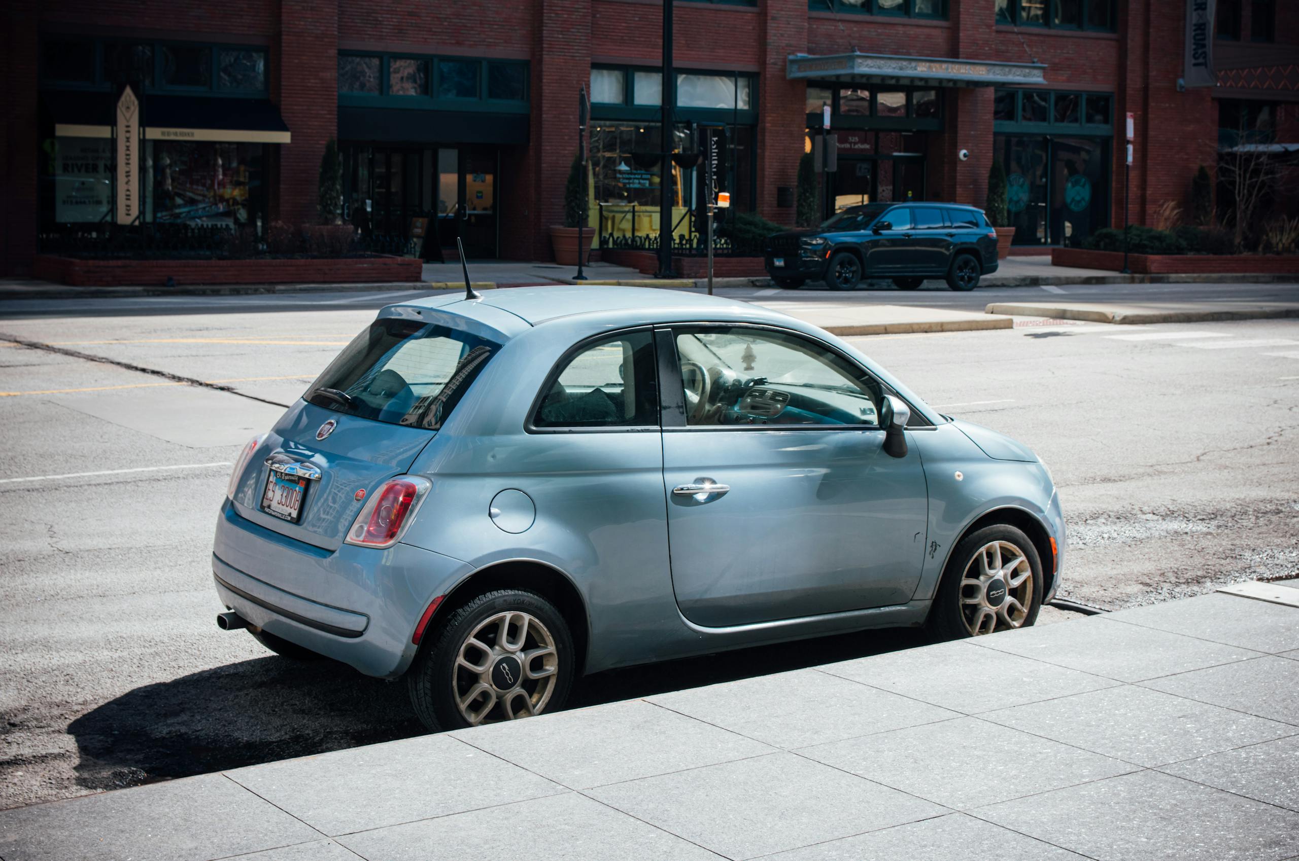 Blue Fiat 500 parked on a Chicago street with brick building backdrop.
