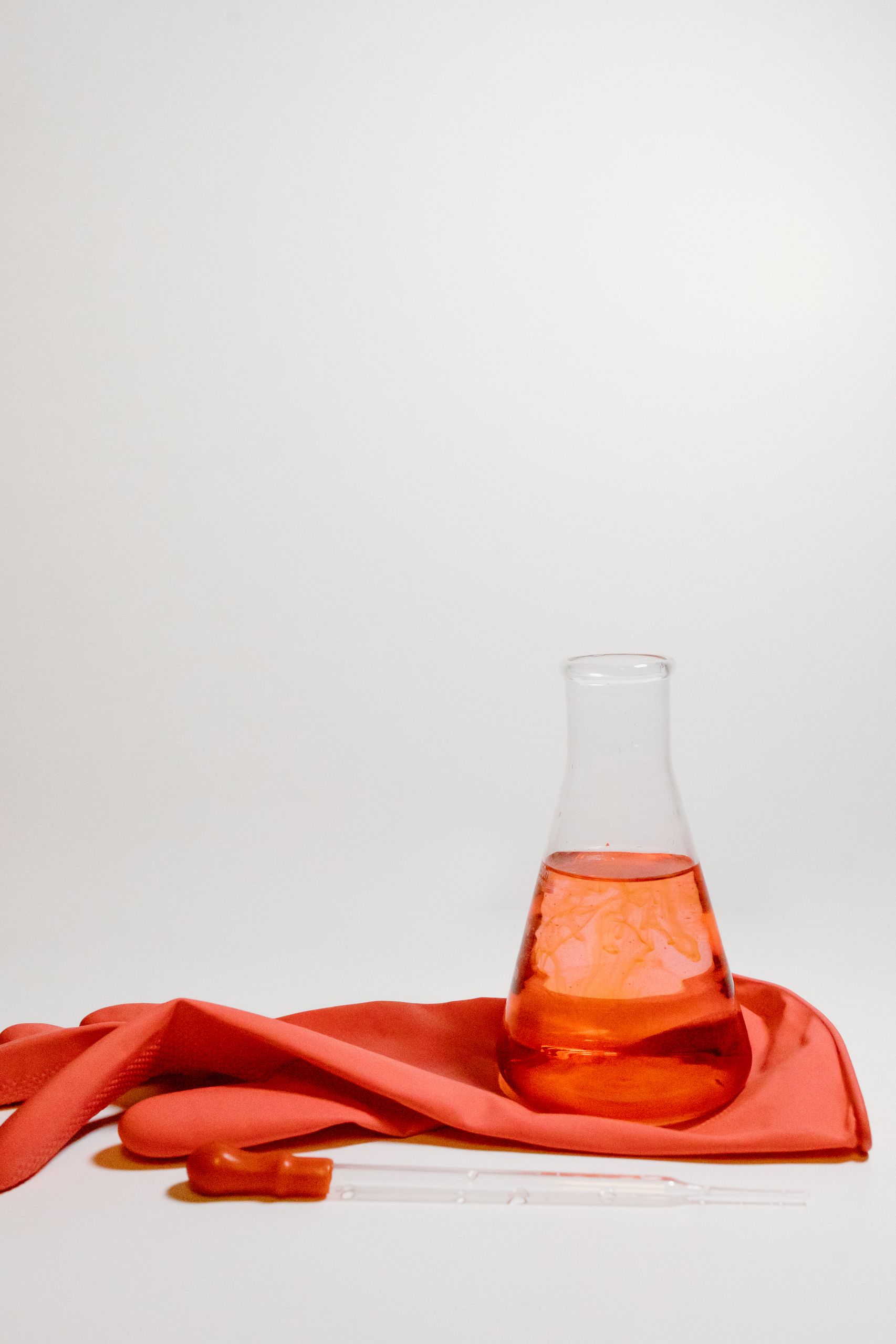 Bright orange lab setup with Erlenmeyer flask, gloves, and pipette on white background.