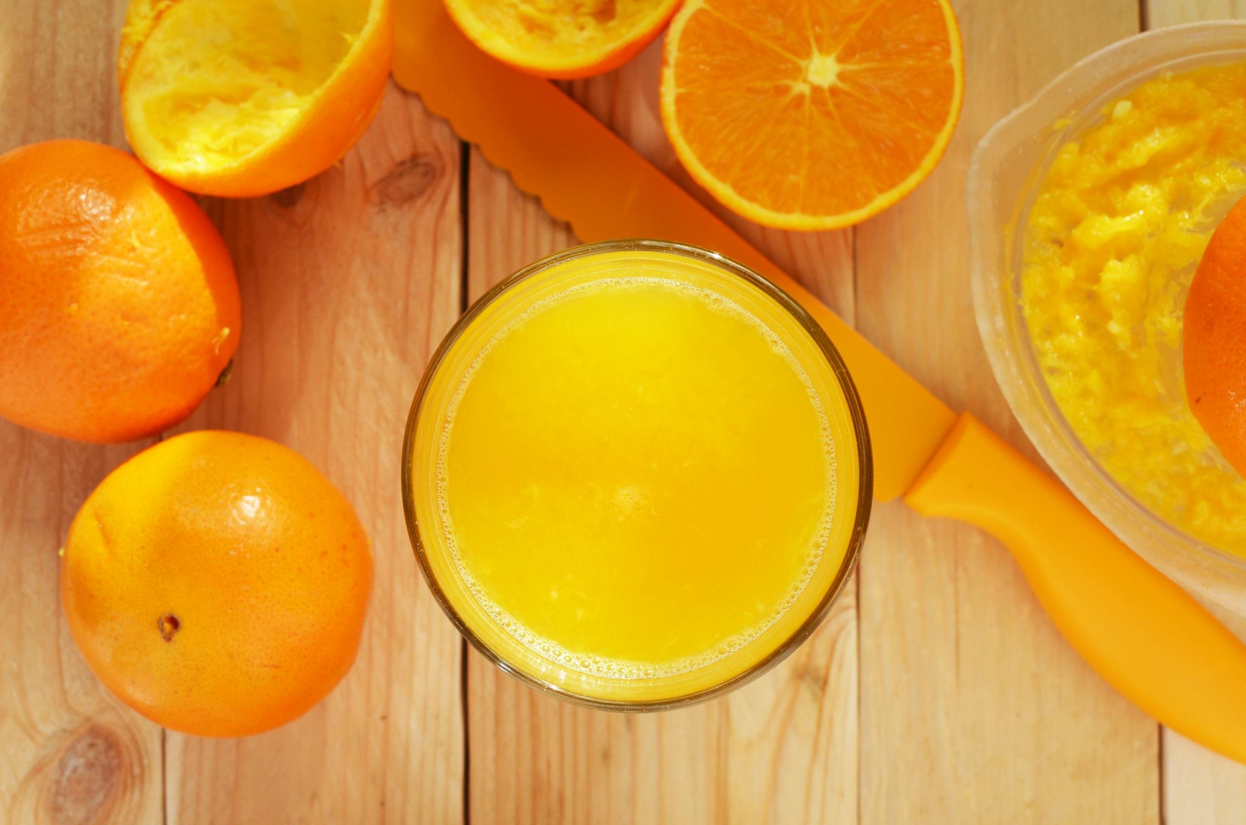 Bright overhead shot of fresh orange juice and oranges on a wooden table, symbolizing health and freshness.