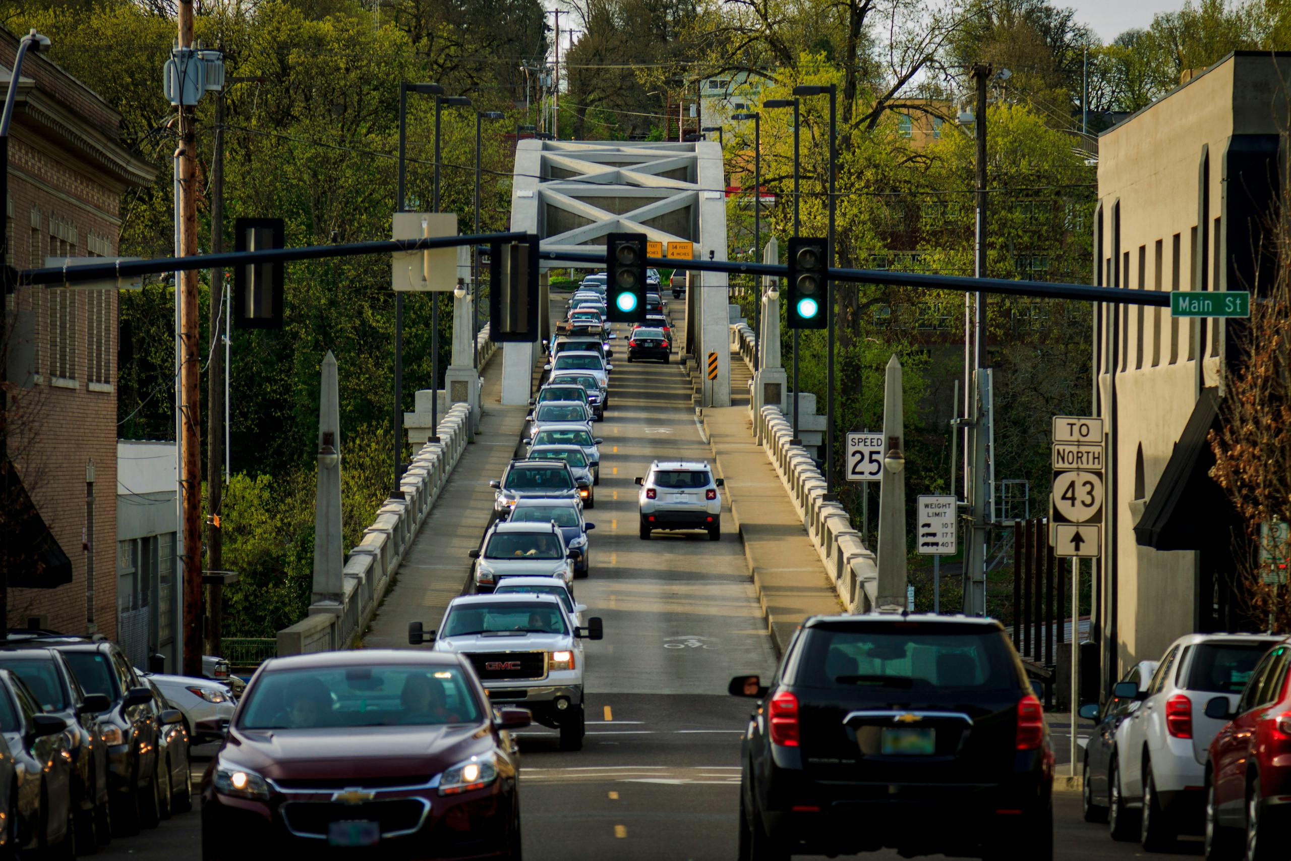 Cars crossing a historic bridge in Oregon City, highlighted by vibrant greenery and urban surroundings.