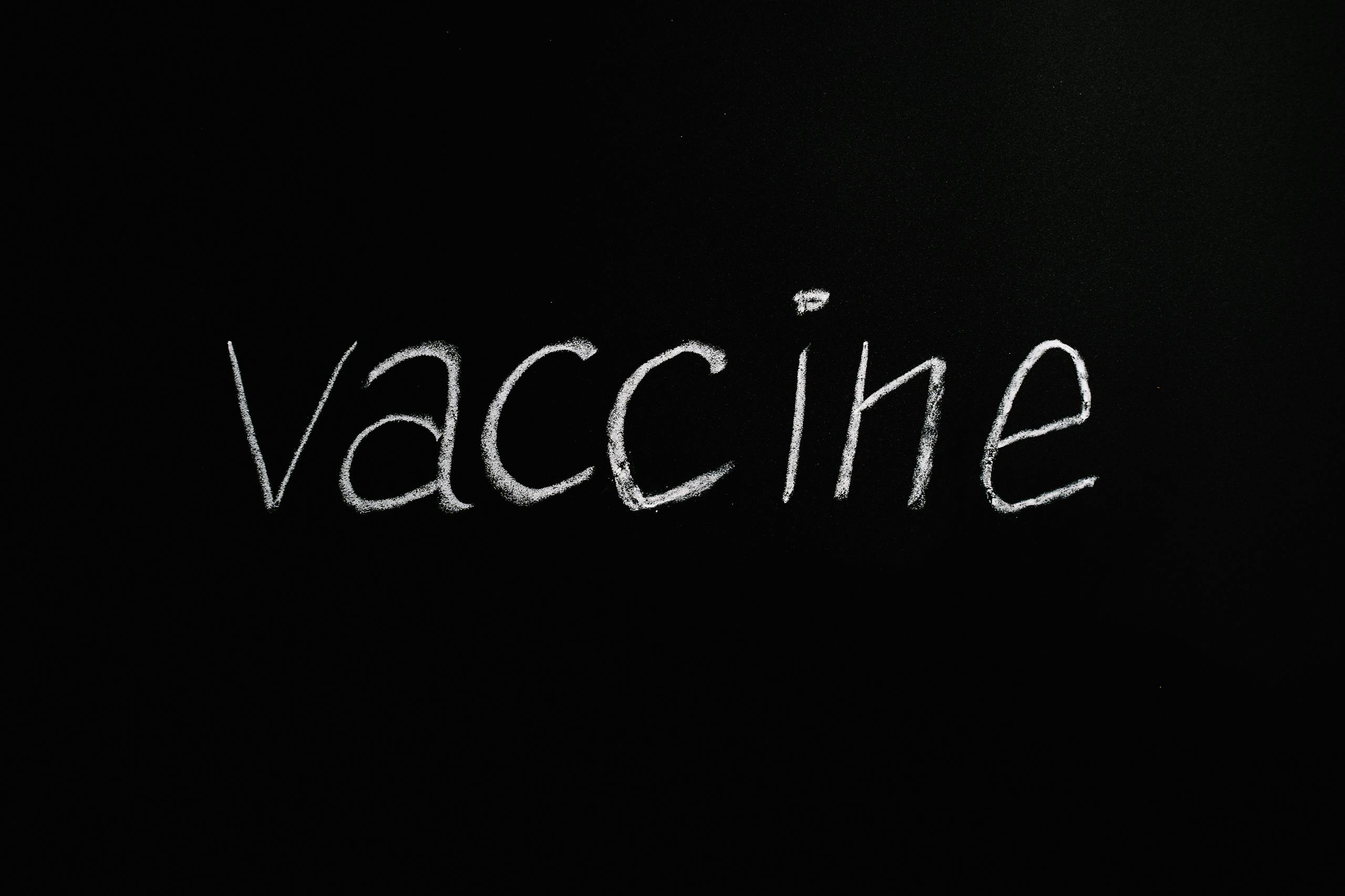 Chalk-drawn word 'vaccine' on blackboard representing health and prevention.