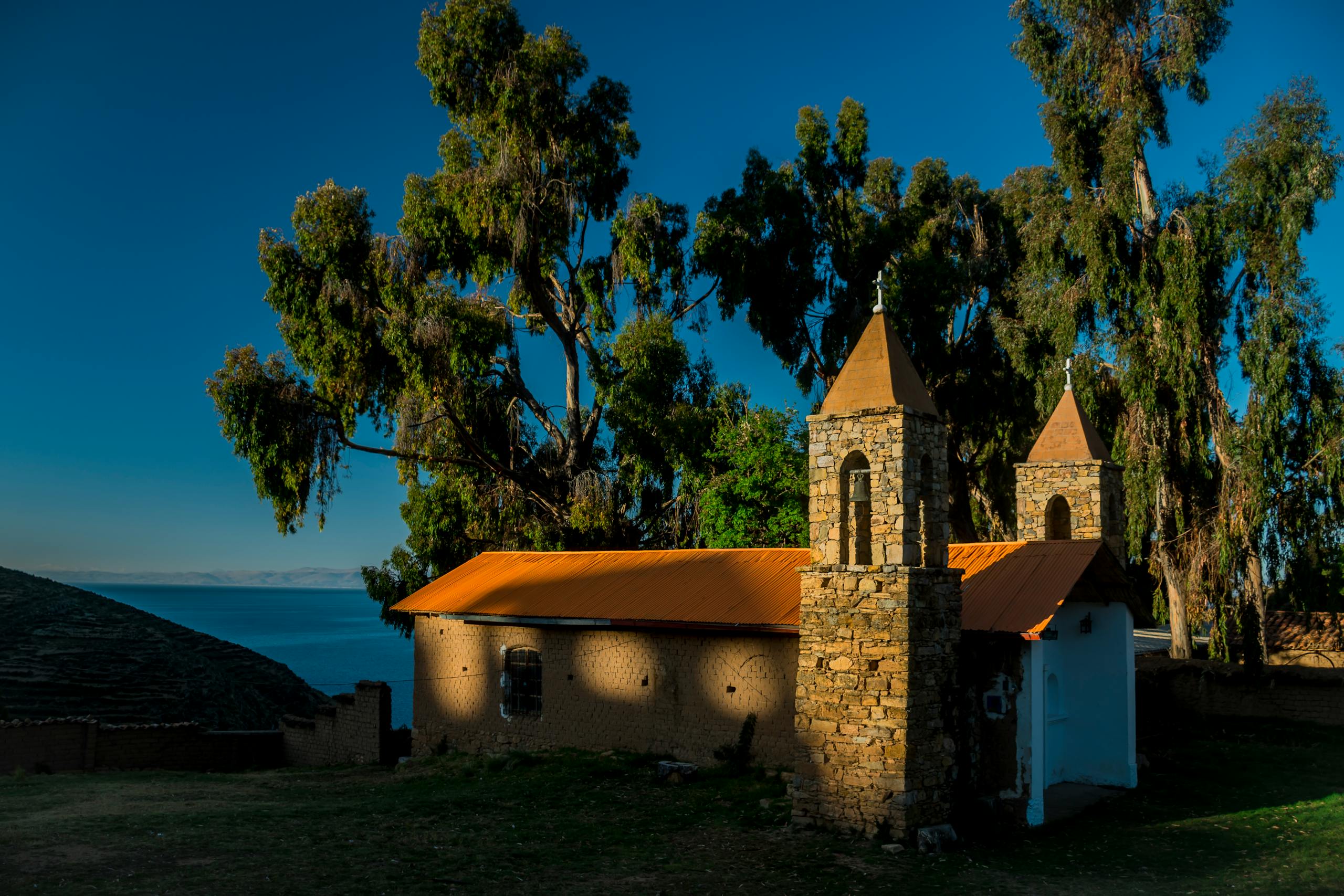 Charming stone chapel surrounded by trees on the shores of Lake Titicaca under the warm sunlight.