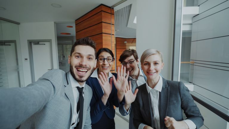 Cheerful business team smiling and waving at the camera indoors.