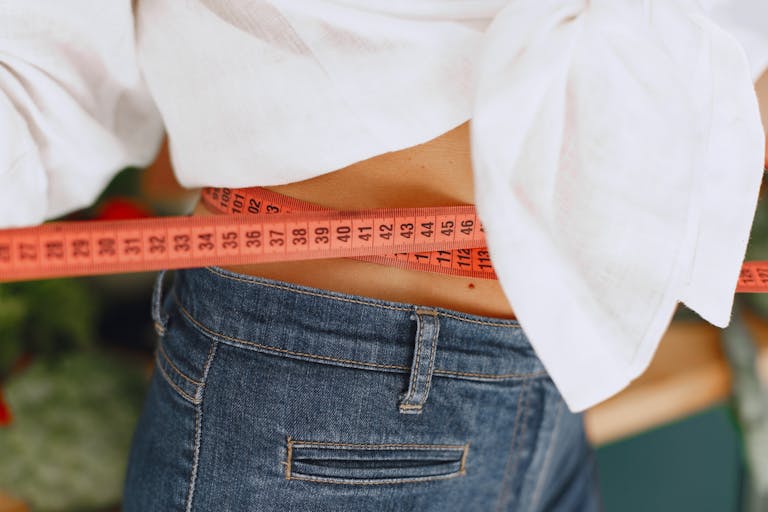 Close-up image of a woman measuring her waist with a tape measure, promoting fitness and health goals.