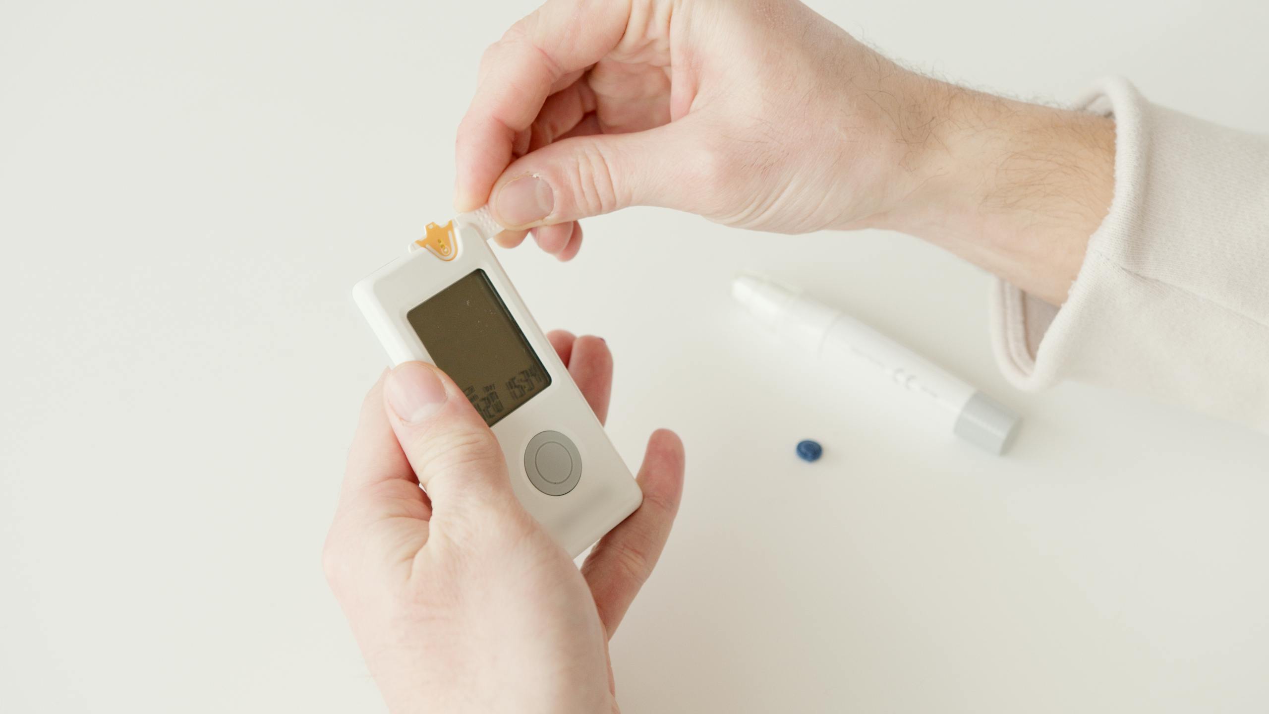 Close-up image of hands checking blood glucose level using a glucometer, featuring testing supplies on a white background.