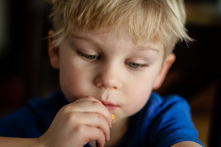 Close-up of a blonde child eating a snack, focused and thoughtful.
