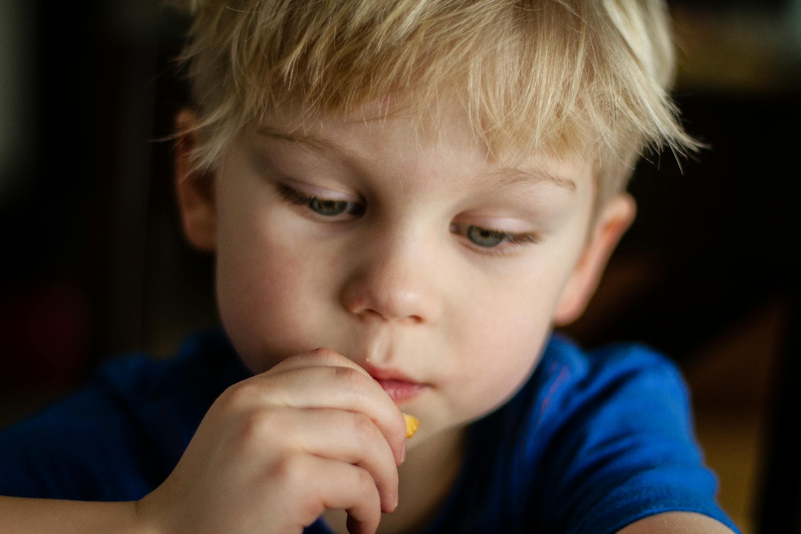 Close-up of a blonde child eating a snack, focused and thoughtful.