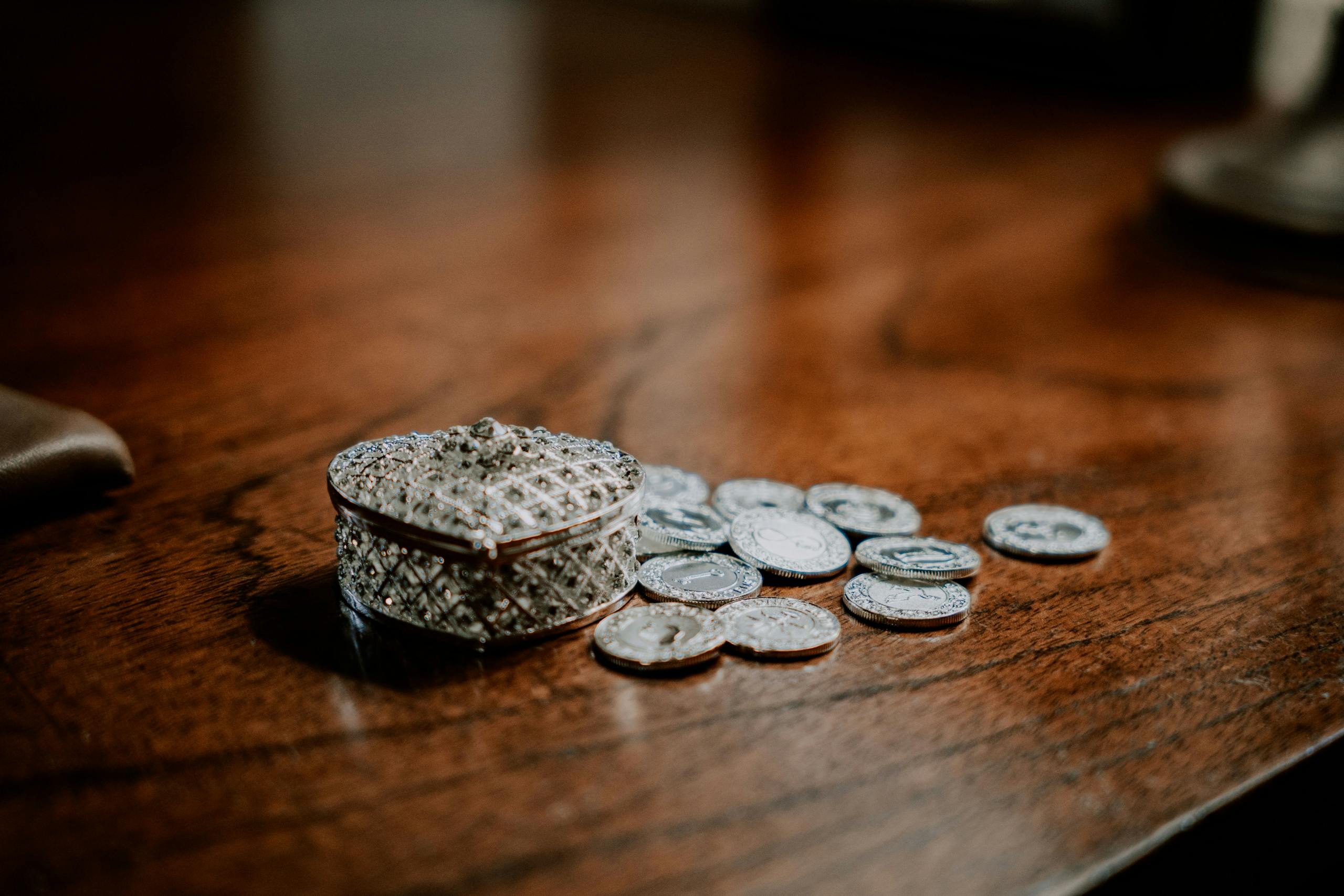 Close-up of a decorative heart-shaped box with scattered coins on a wooden surface.