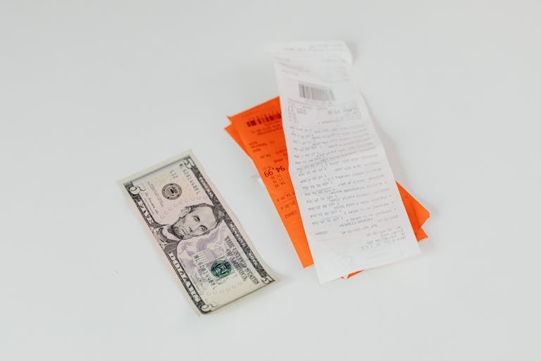 Close-up of a five-dollar bill next to shopping receipts on a white background, ideal for finance and retail themes.