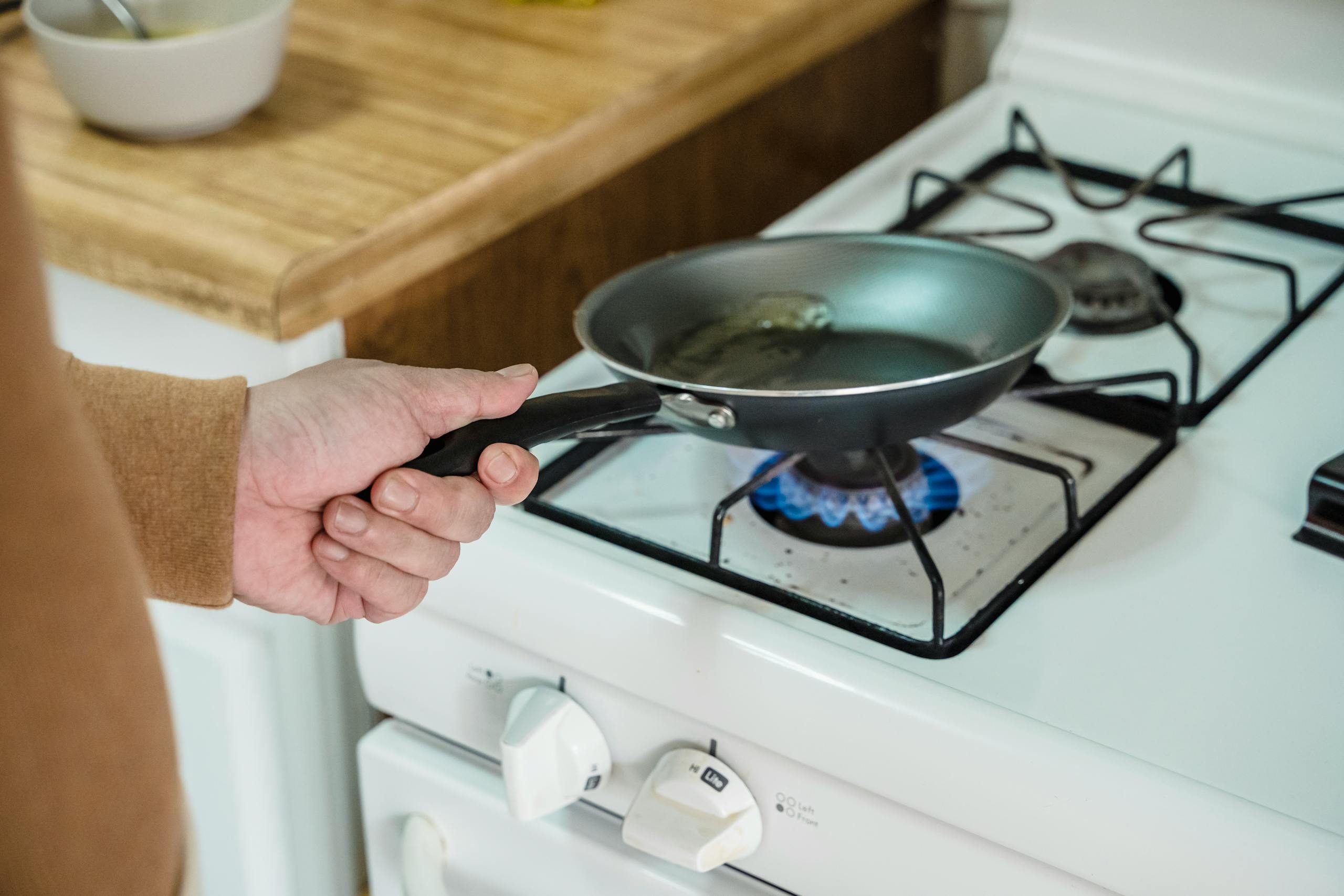 Close-up of a hand holding a frying pan over a gas burner in a kitchen